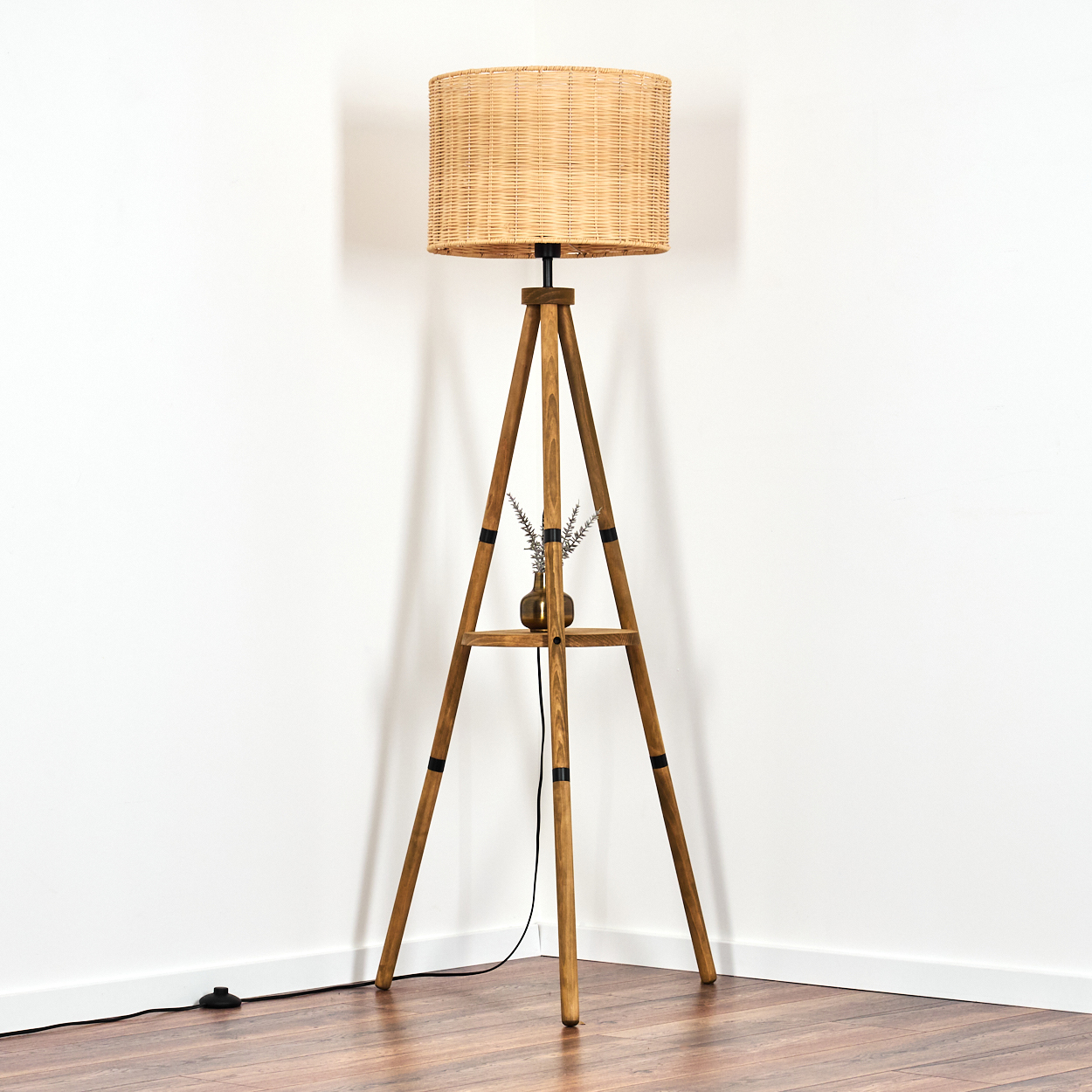 Ein Stehlampenfuß aus Holz mit einem Lampenschirm aus Rattan, daneben eine kleine Vase mit Zweigen.