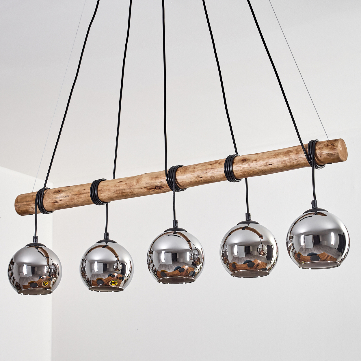 Fünf kugelförmige, spiegelnde Lampen hängen von einem Holzbalken.
