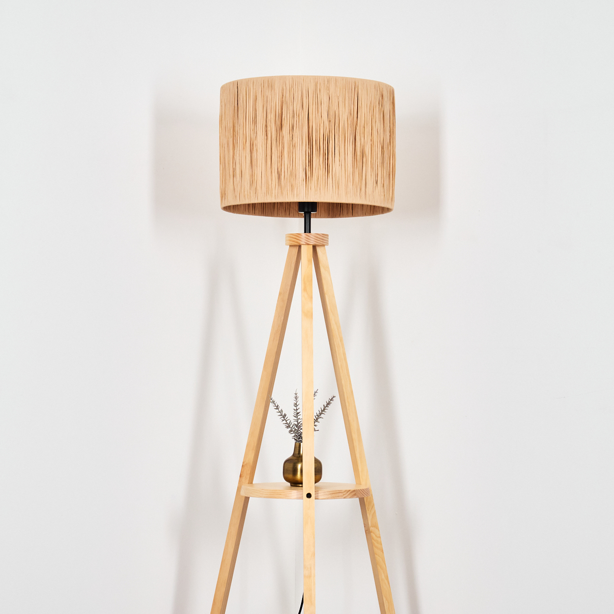 Ein Holz-Stehleuchte mit einem geflochtenen Lampenschirm und einem kleinen goldenen Vasenaufsteller.