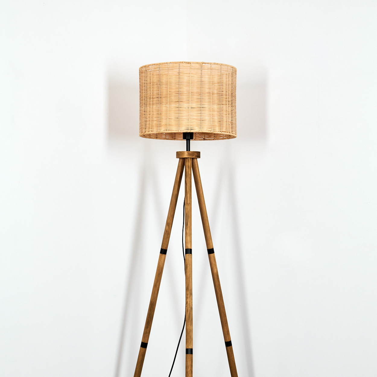 Eine Stehlampe mit einem geflochtenen Korbschirm und einem Holzstativ.
