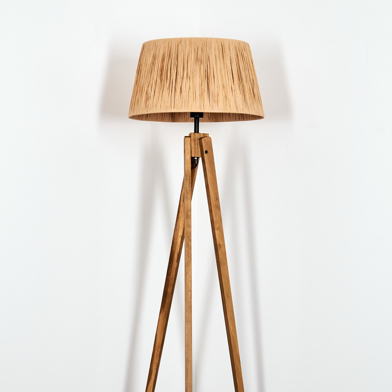 Ein Stehleuchte mit einem Lampenschirm aus Bast und einem Holzstativ vor einer weißen Wand.