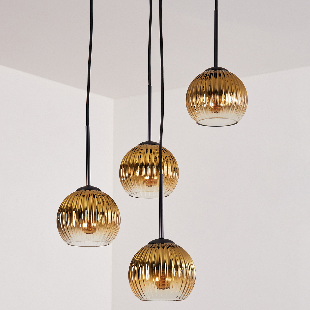 Vier goldene, gerippte Pendelleuchten mit schwarzen Kabeln hängen von der Decke.