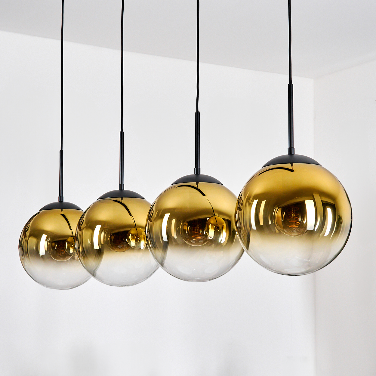Vier goldene Glaskugelleuchten hängen an schwarzen Kabeln.