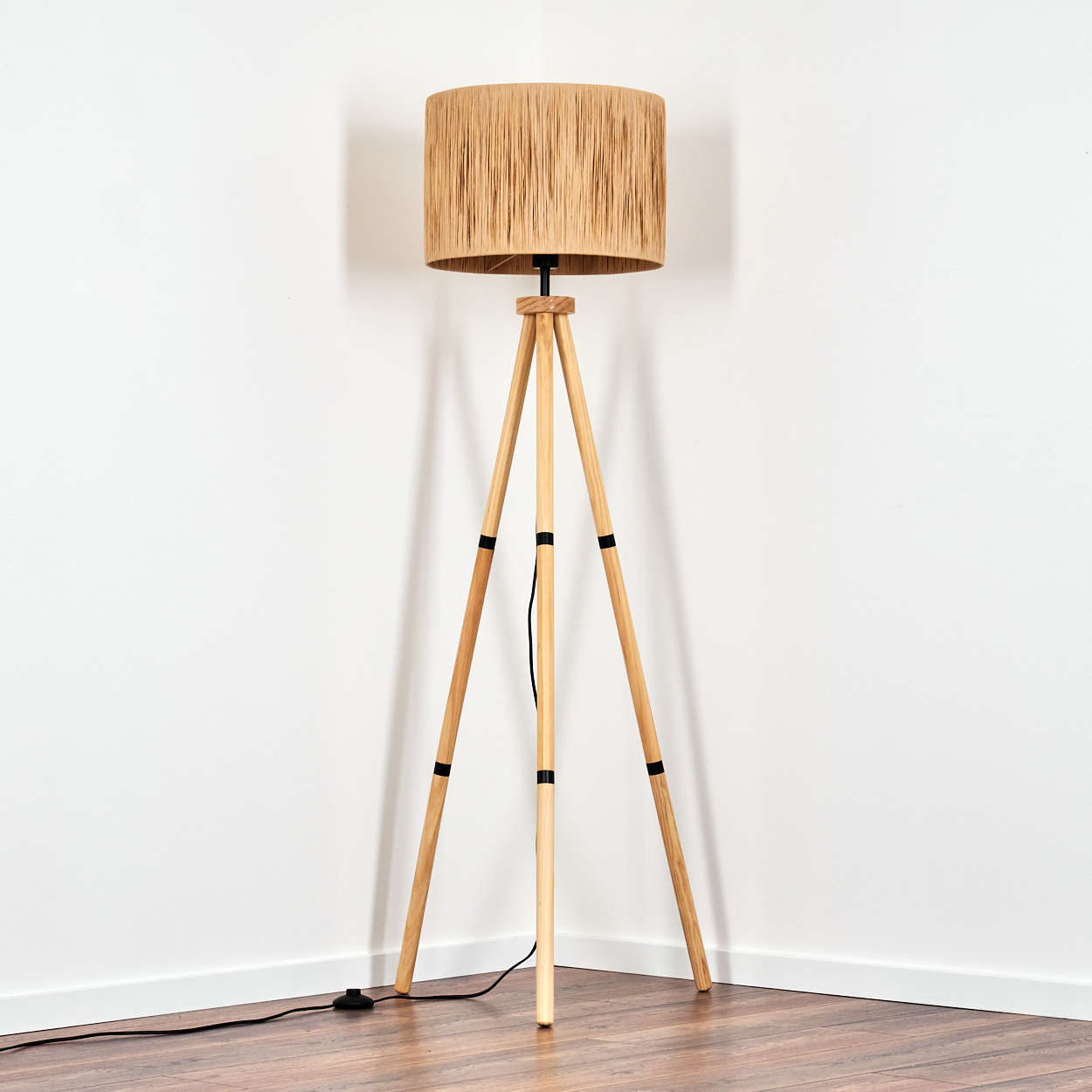 Ein Stehlampen-Stativ aus Holz mit einem geflochtenen Lampenschirm steht in einer Ecke.