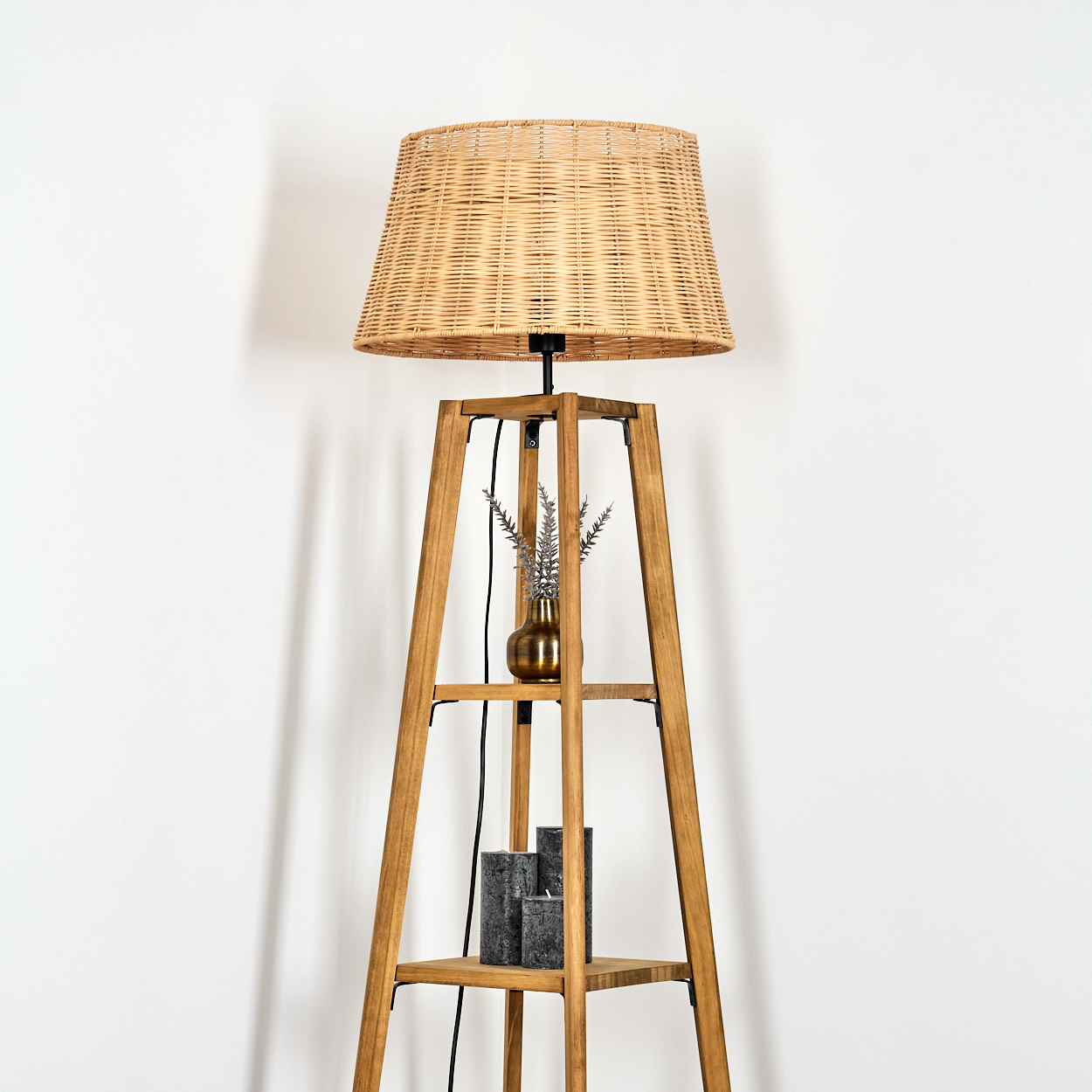 Ein Holzbodenständer mit einem geflochtenen Lampenschirm, Vase mit Zweigen und Kerzen.