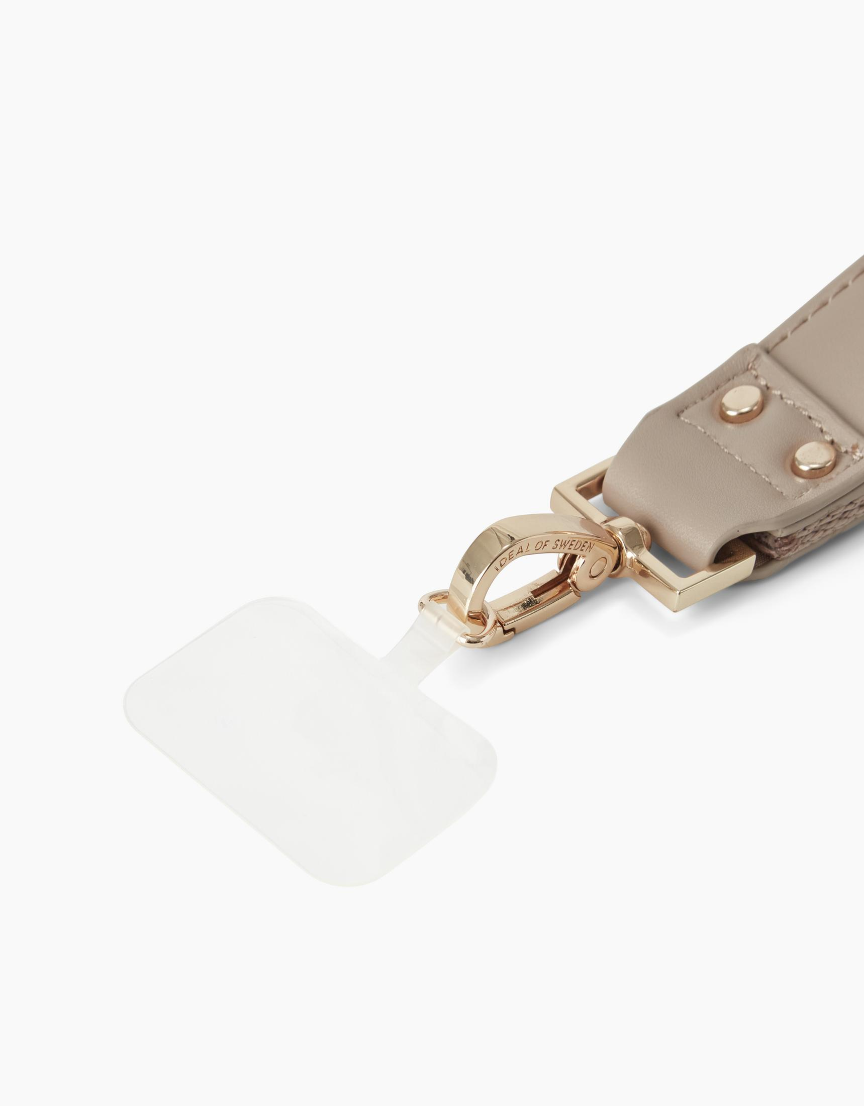 Ein beiger Gurt mit goldenen Beschlägen und einem transparenten Anhänger.