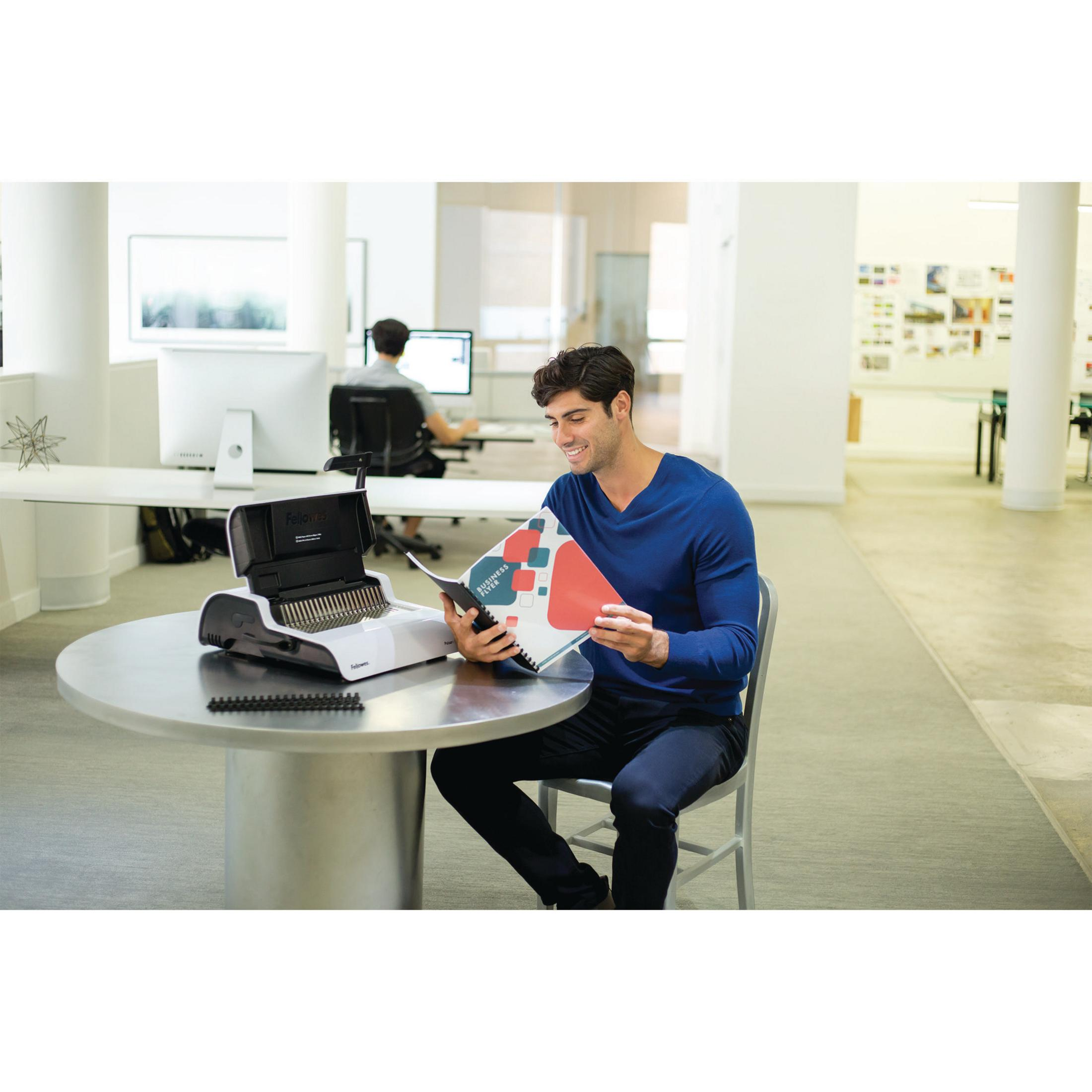 Man reads a booklet next to a binding machine at a round table.