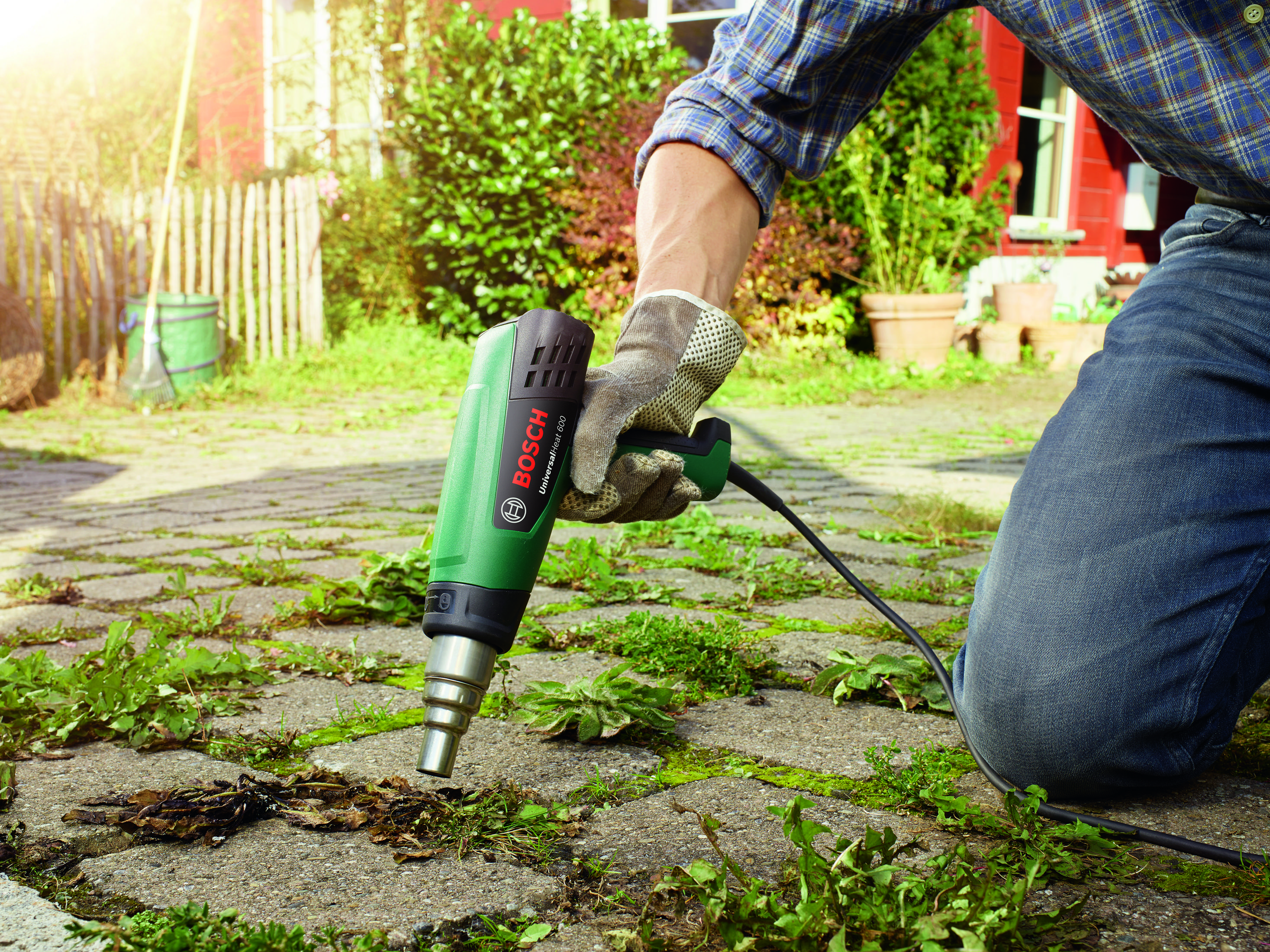 Dispositivo Bosch verde in mano, puntato verso un'area pavimentata con erbacce.