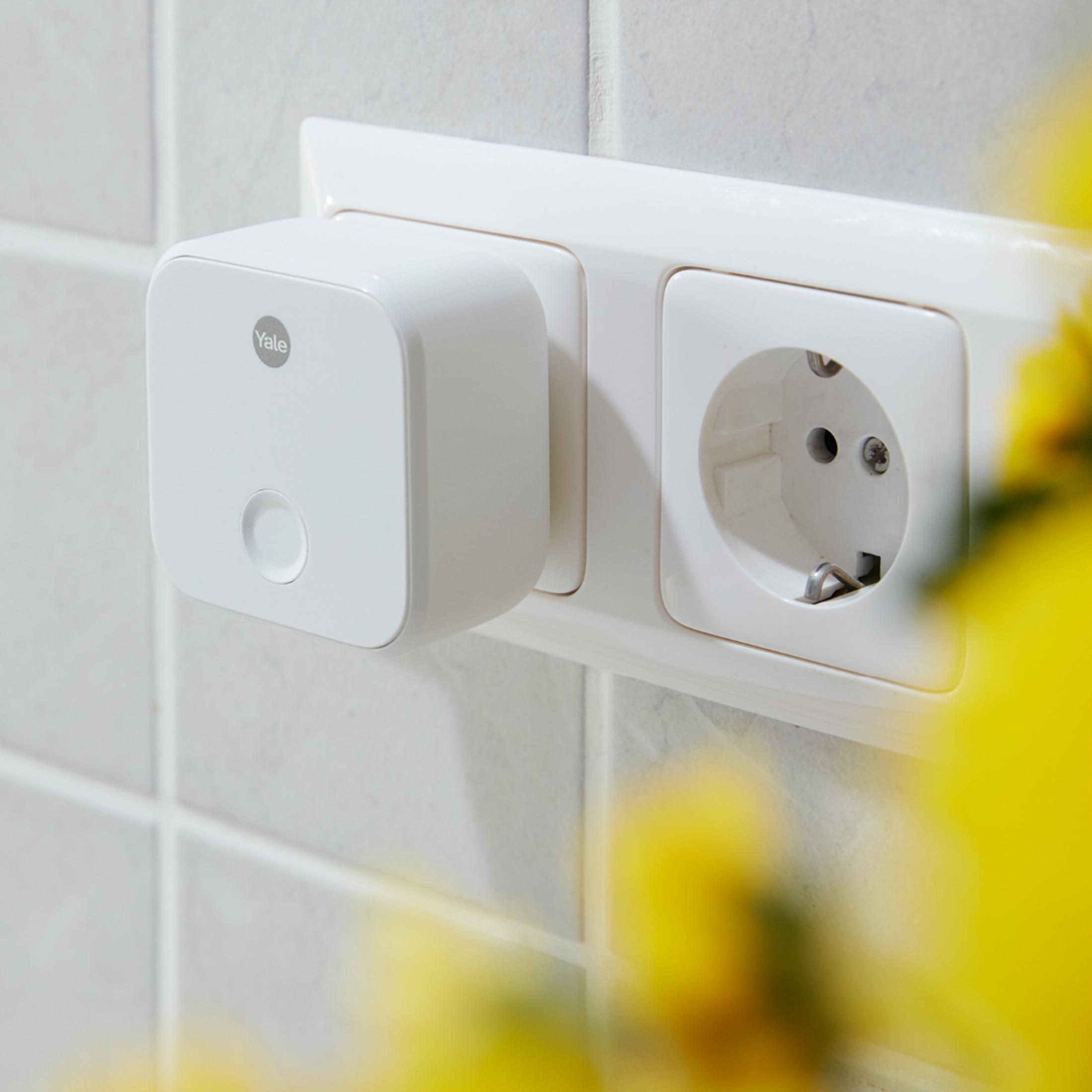 Un adattatore Yale bianco è inserito in una presa a muro accanto a una presa vuota.
