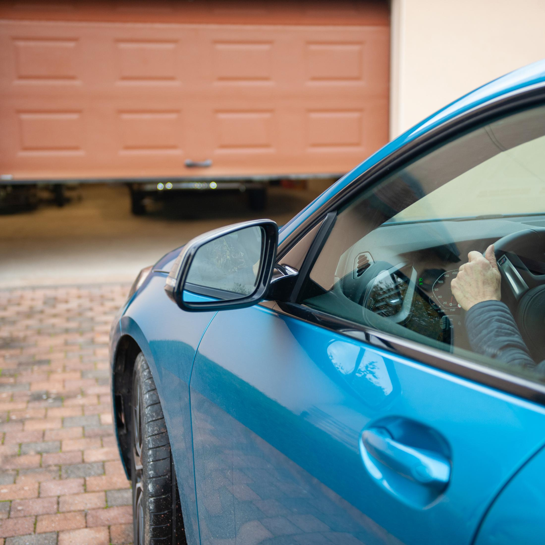 Un'auto blu si dirige verso un garage, le mani del conducente sul volante.