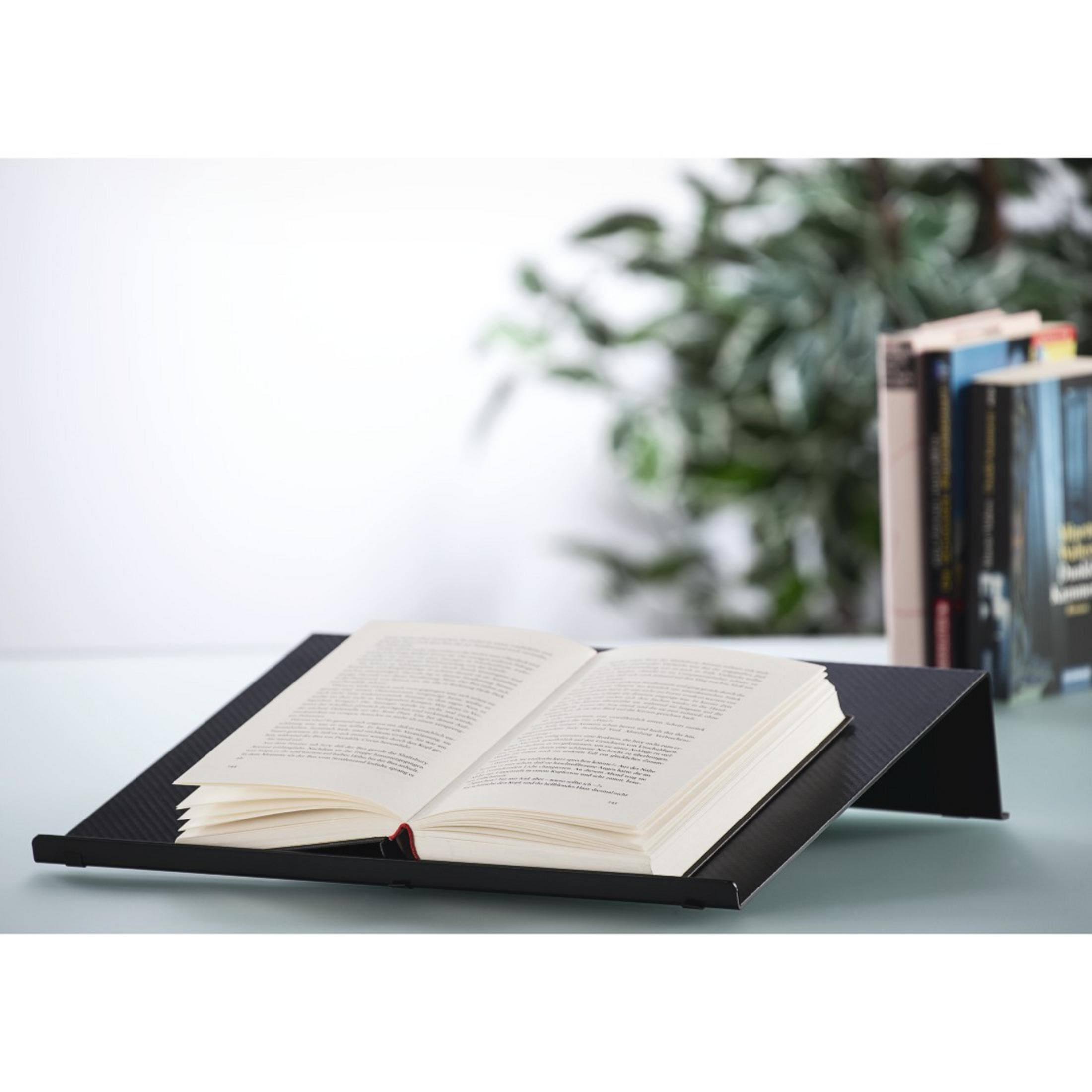 Ein offenes Buch liegt auf einem schwarzen Ständer, im Hintergrund Bücher und Pflanzen.