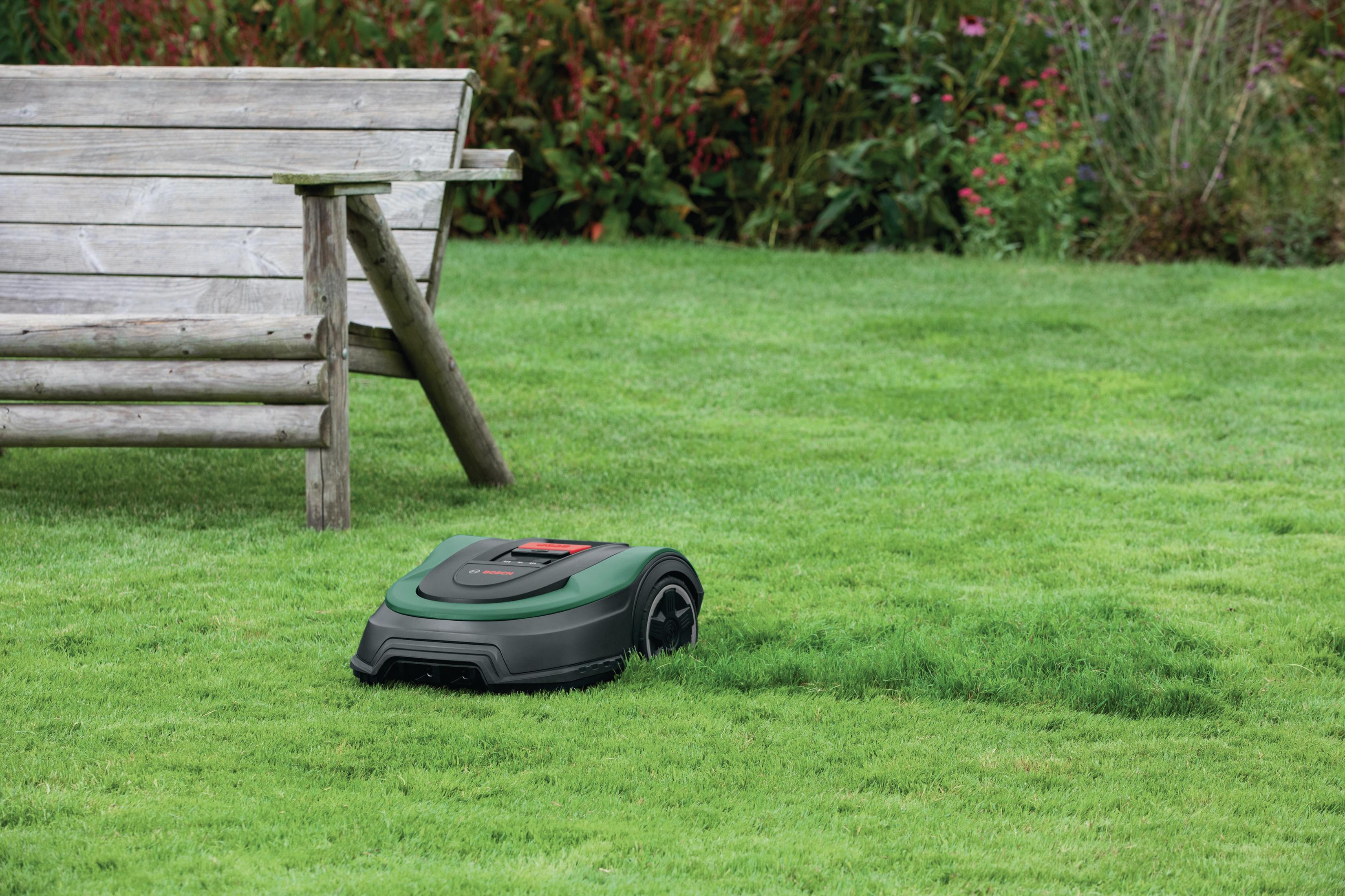 Ein Mähroboter steht auf einem grünen Rasen neben einer Holzbank.