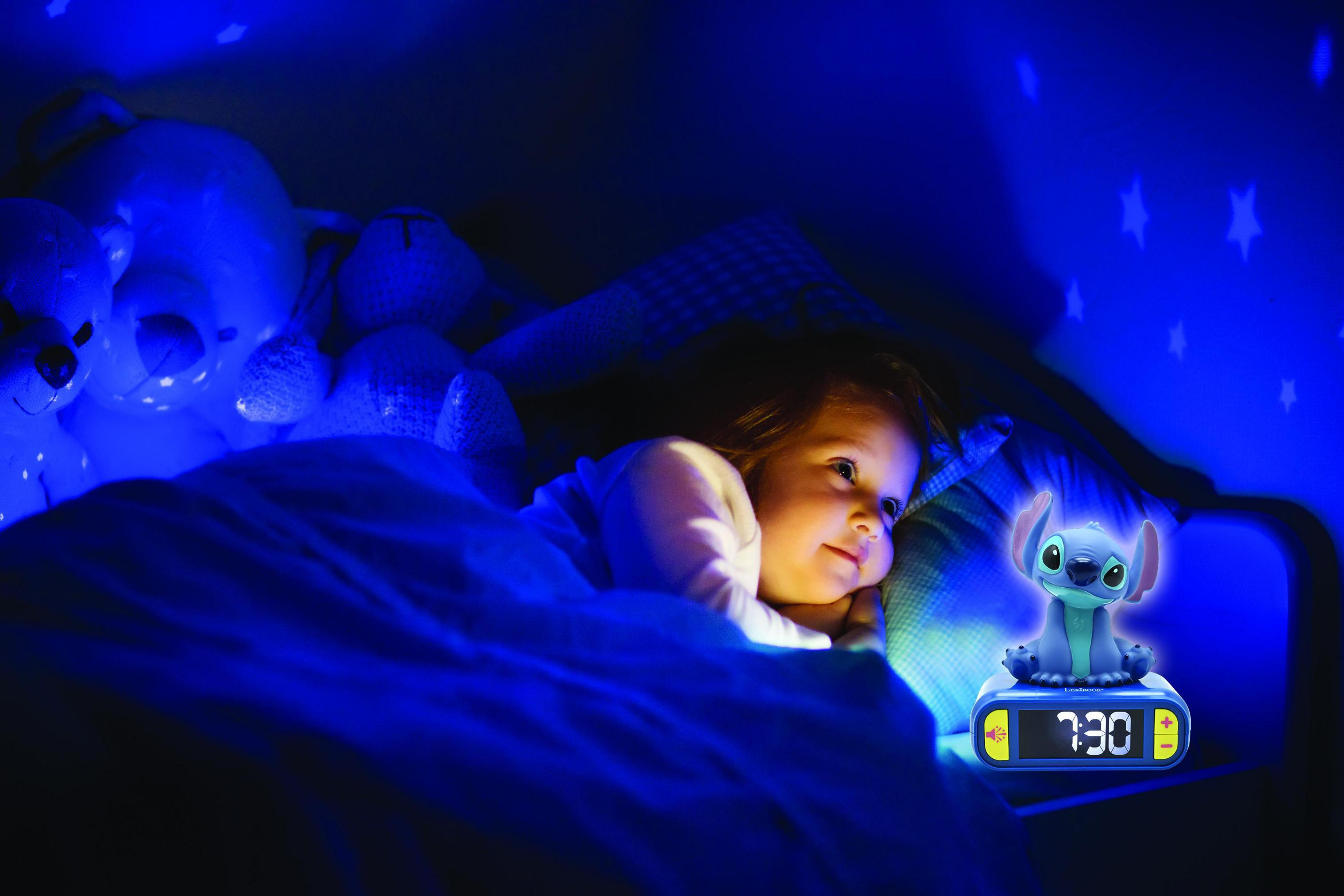 Kind im Bett mit Stofftieren und einer blauen Sternenlicht-Projektion. Ein Wecker zeigt 7:30.