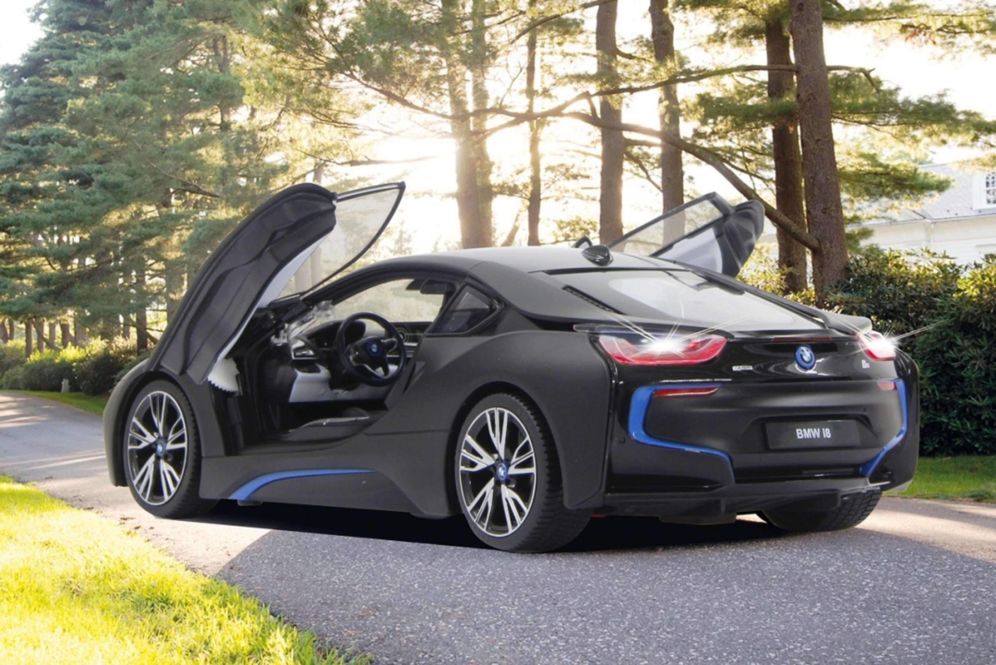 Schwarzer BMW i8 mit geöffneten Flügeltüren auf einer Straße, umgeben von Bäumen und Gras.