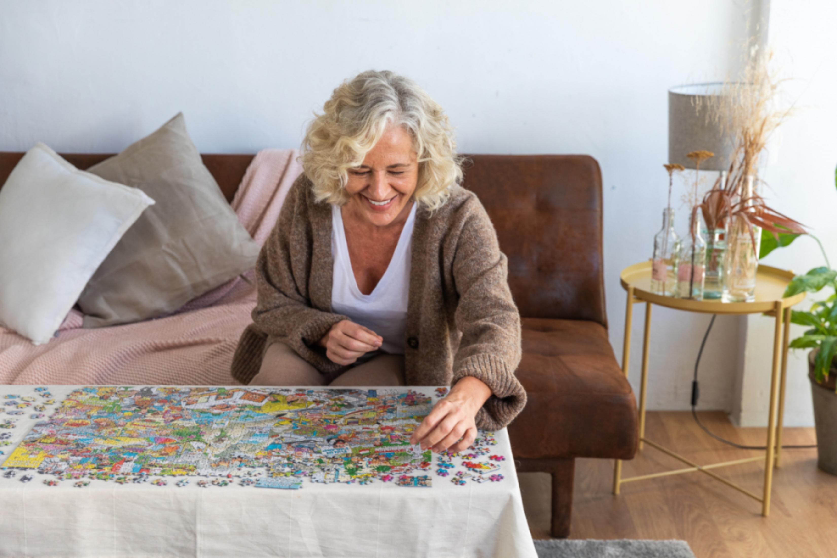 Een vrouw met grijs haar lacht terwijl ze een puzzel legt.