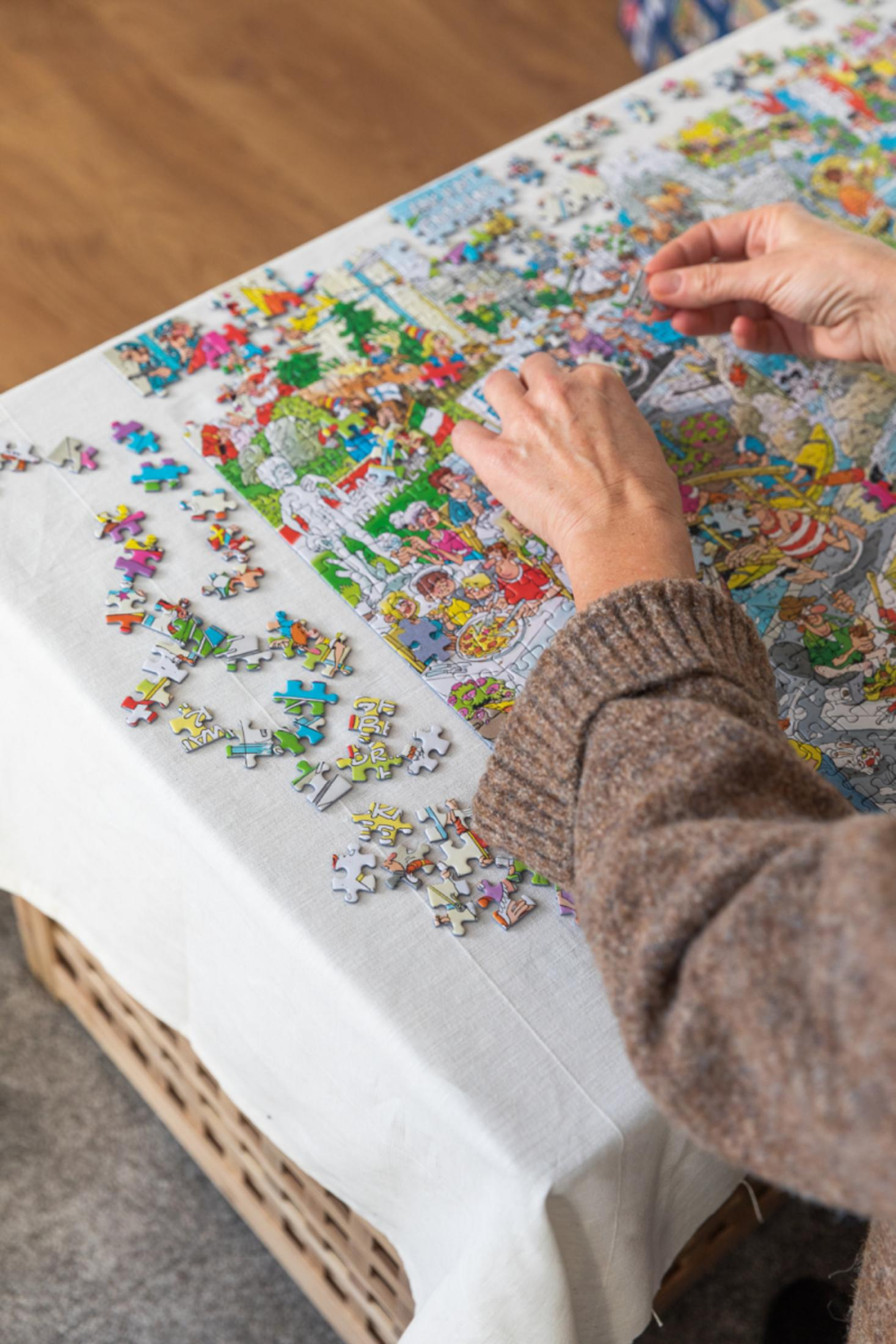 Handen die een kleurrijke legpuzzel leggen op een tafel bedekt met witte stof.