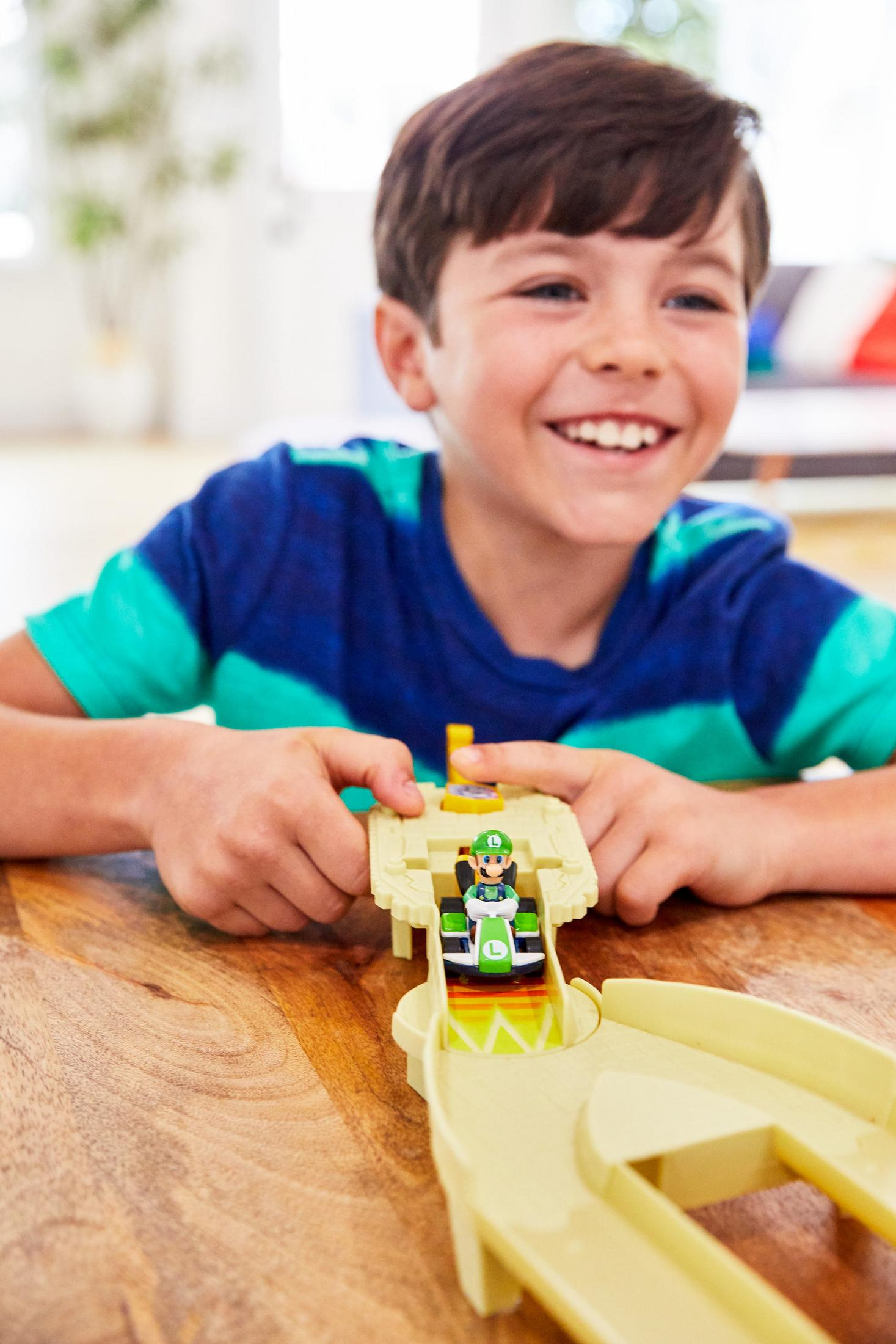 Ein Junge spielt mit einer Luigi-Spielzeugauto-Rennstrecke auf einem Holztisch.