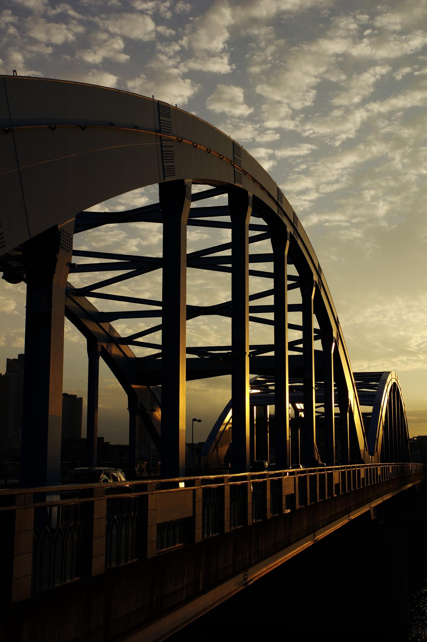 Un puente de arco de acero al atardecer, con nubes en el cielo.