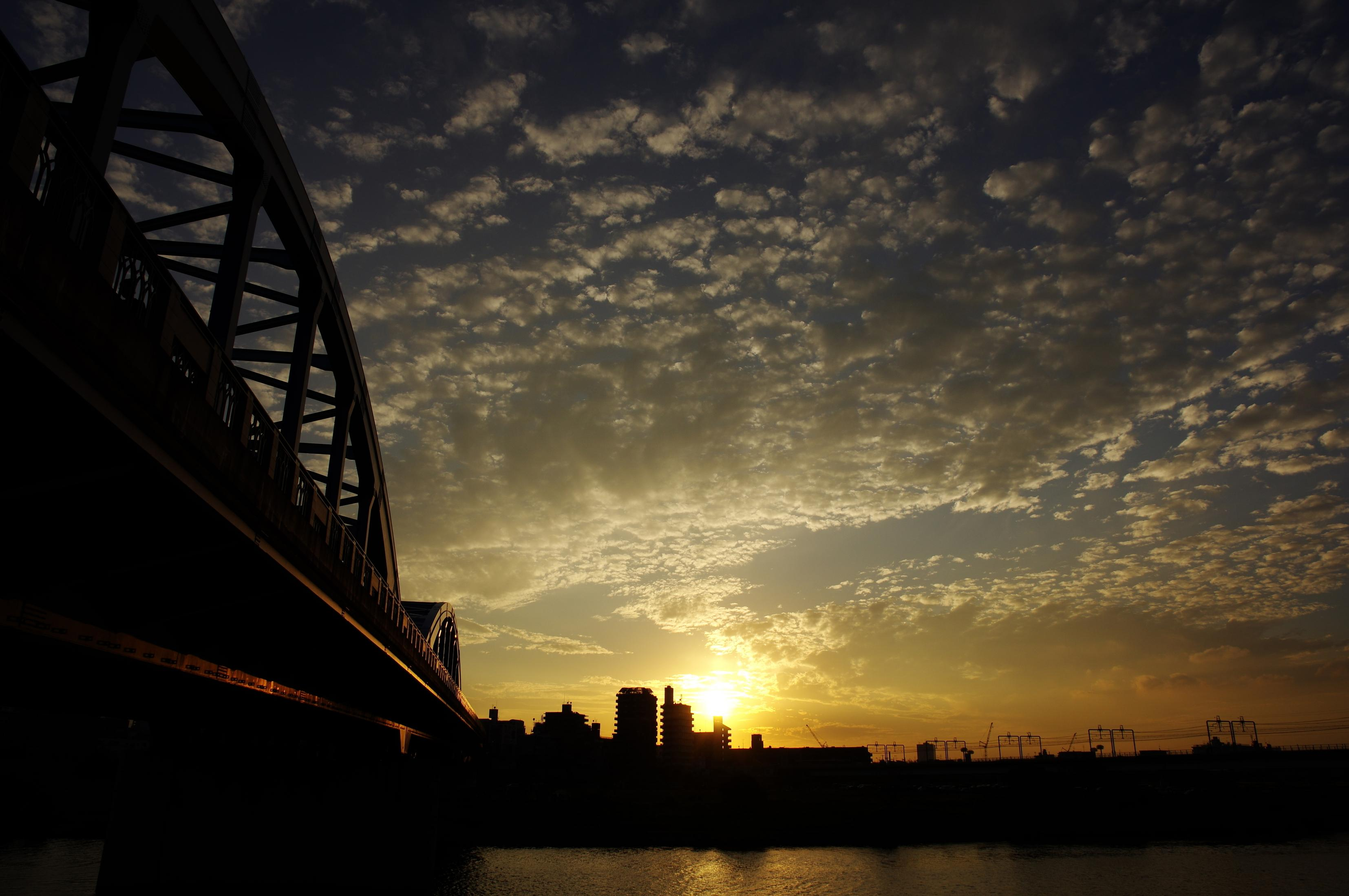 Silueta de un puente sobre un río al atardecer con nubes.