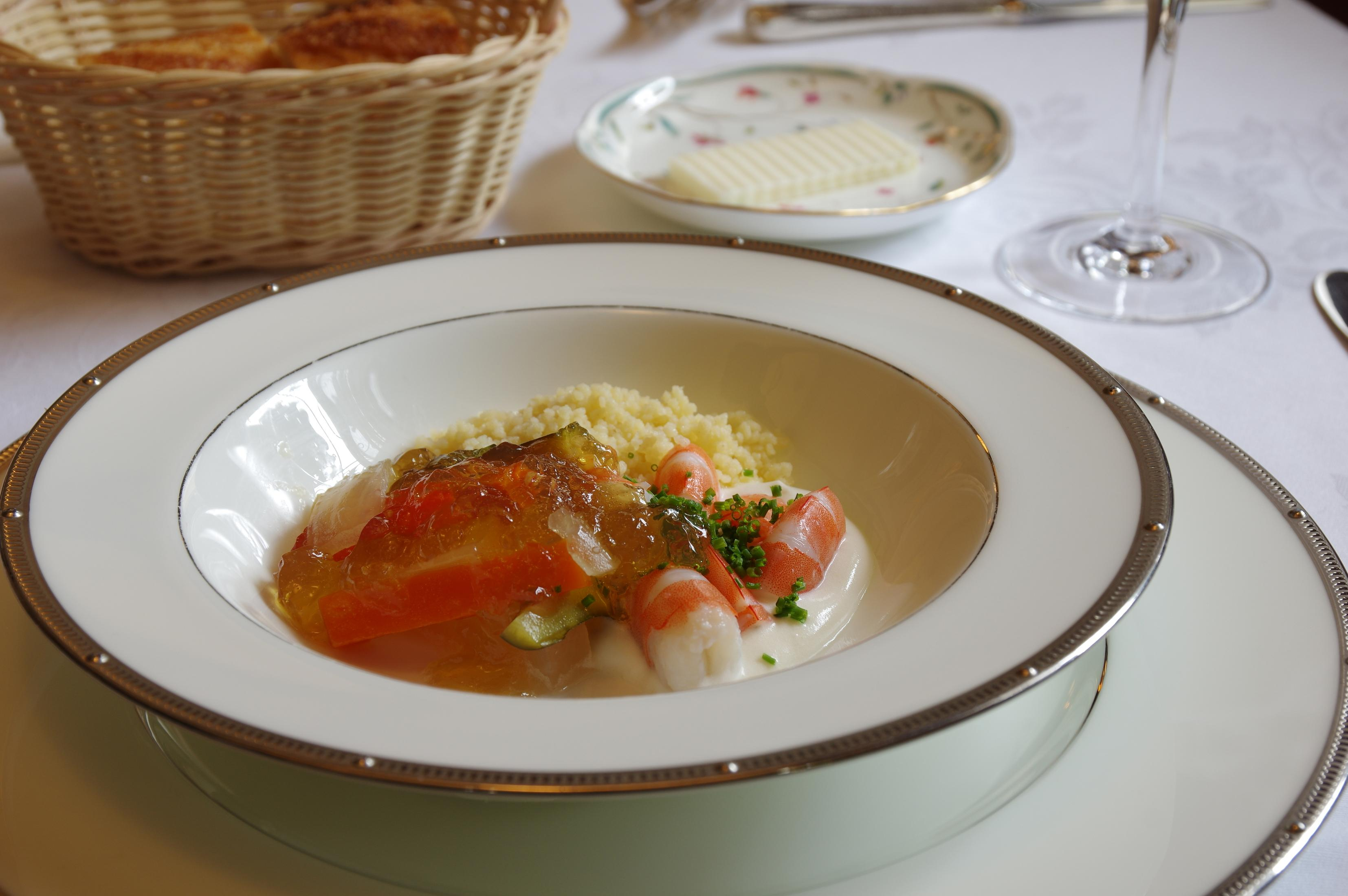 Un bol de cuscús con gambas, gelatina y verduras en un plato blanco.