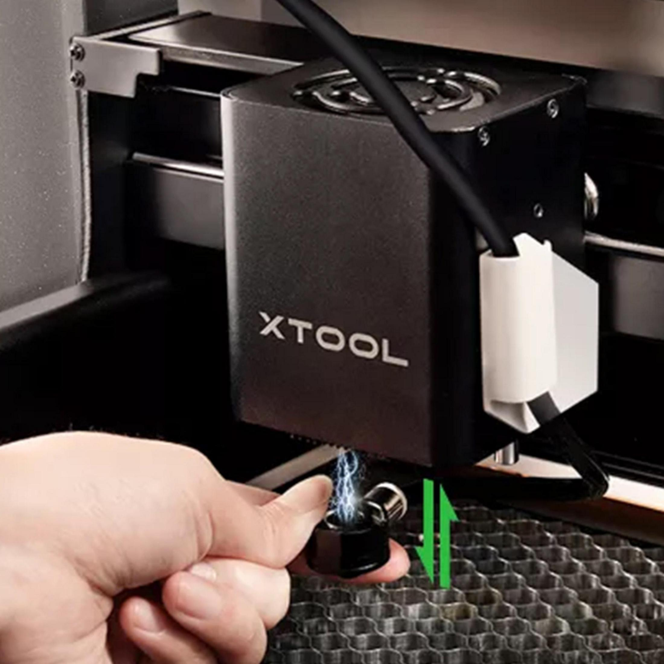 Ein Finger hält ein schwarzes Teil unter einem XTOOL-Laserkopf mit Funken.