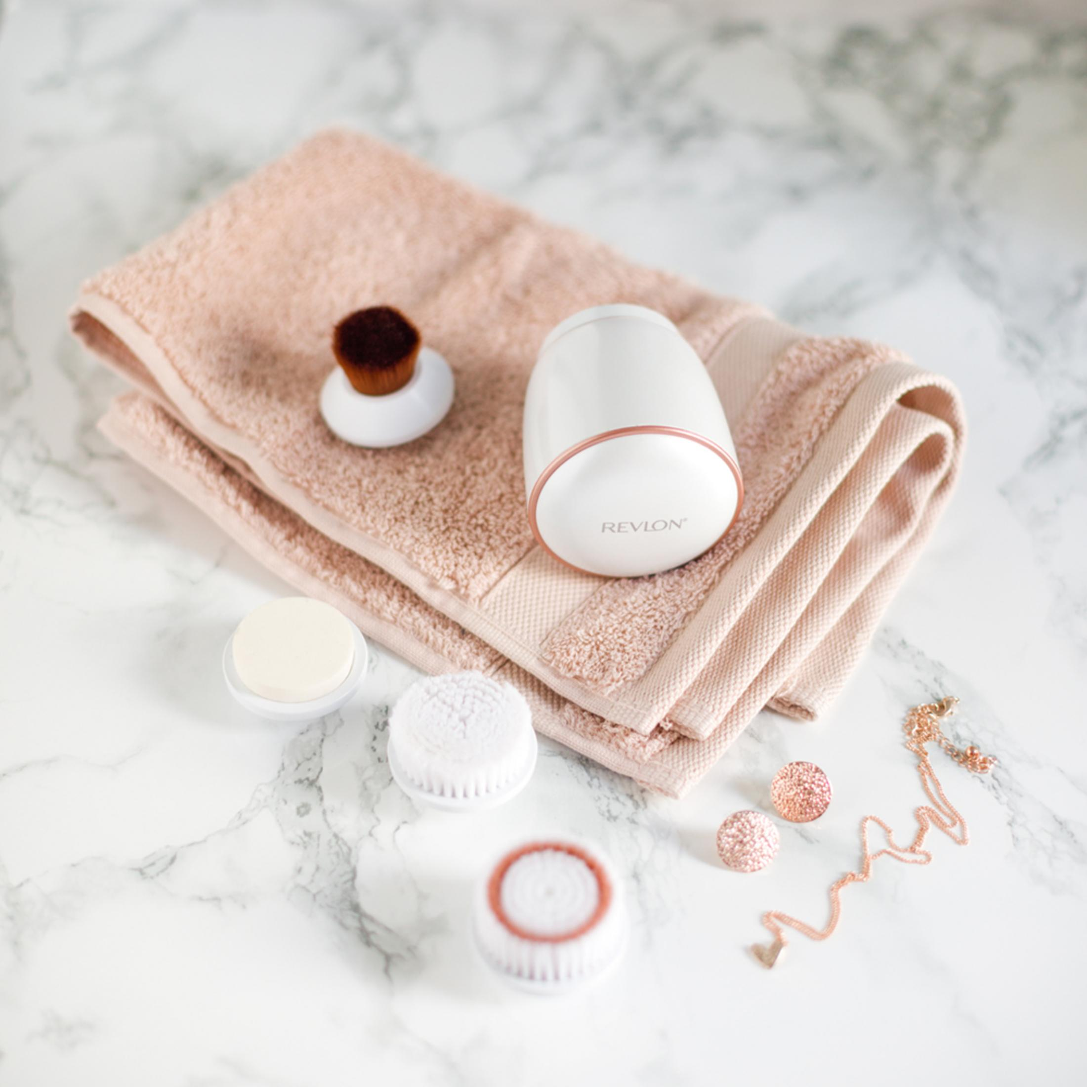 Revlon Gesichtsreinigungsgerät mit Bürsten, Handtuch und Schmuck in Roségold.
