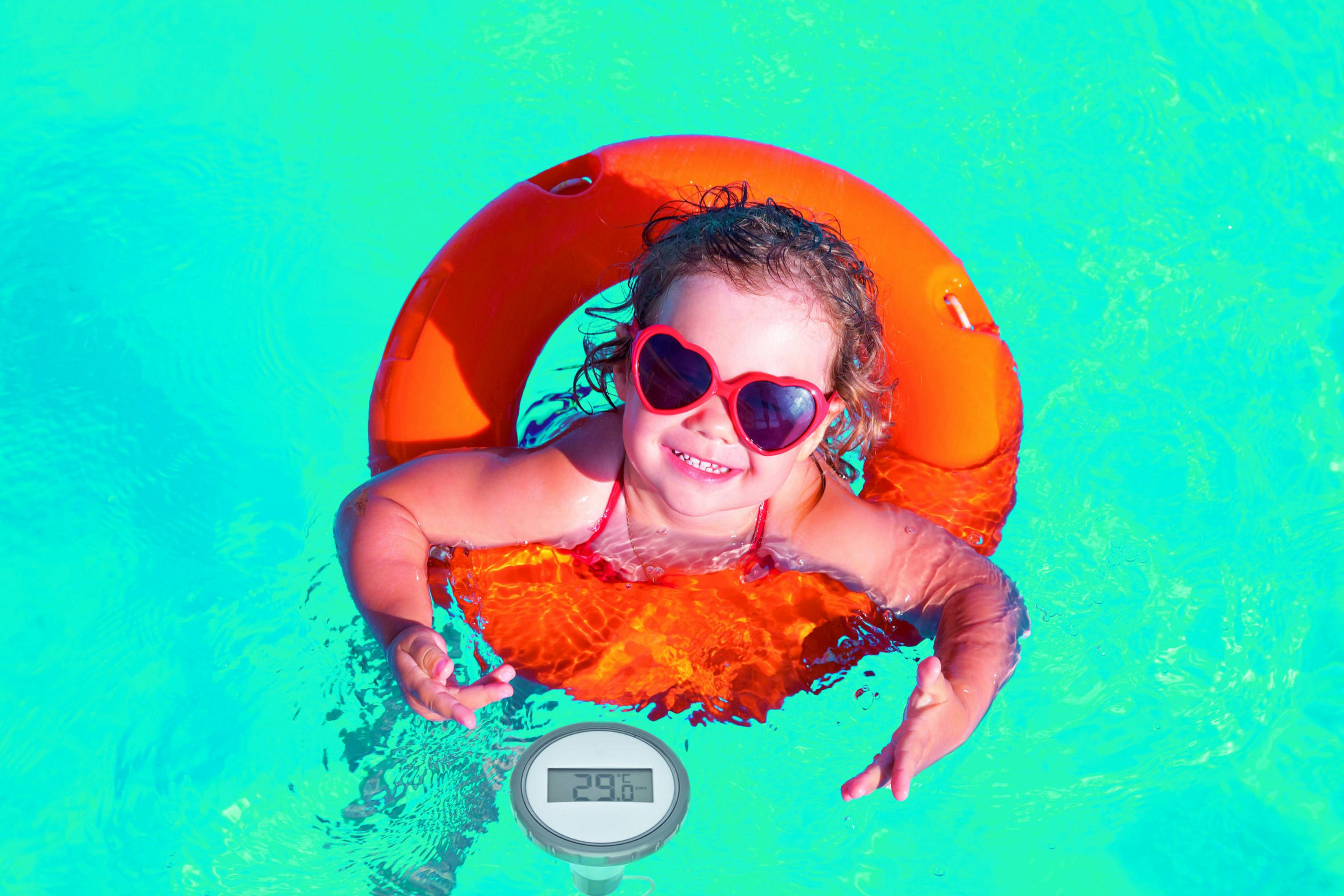 Ein kleines Mädchen mit herzförmiger Sonnenbrille schwimmt in einem orangefarbenen Schwimmring im Pool.