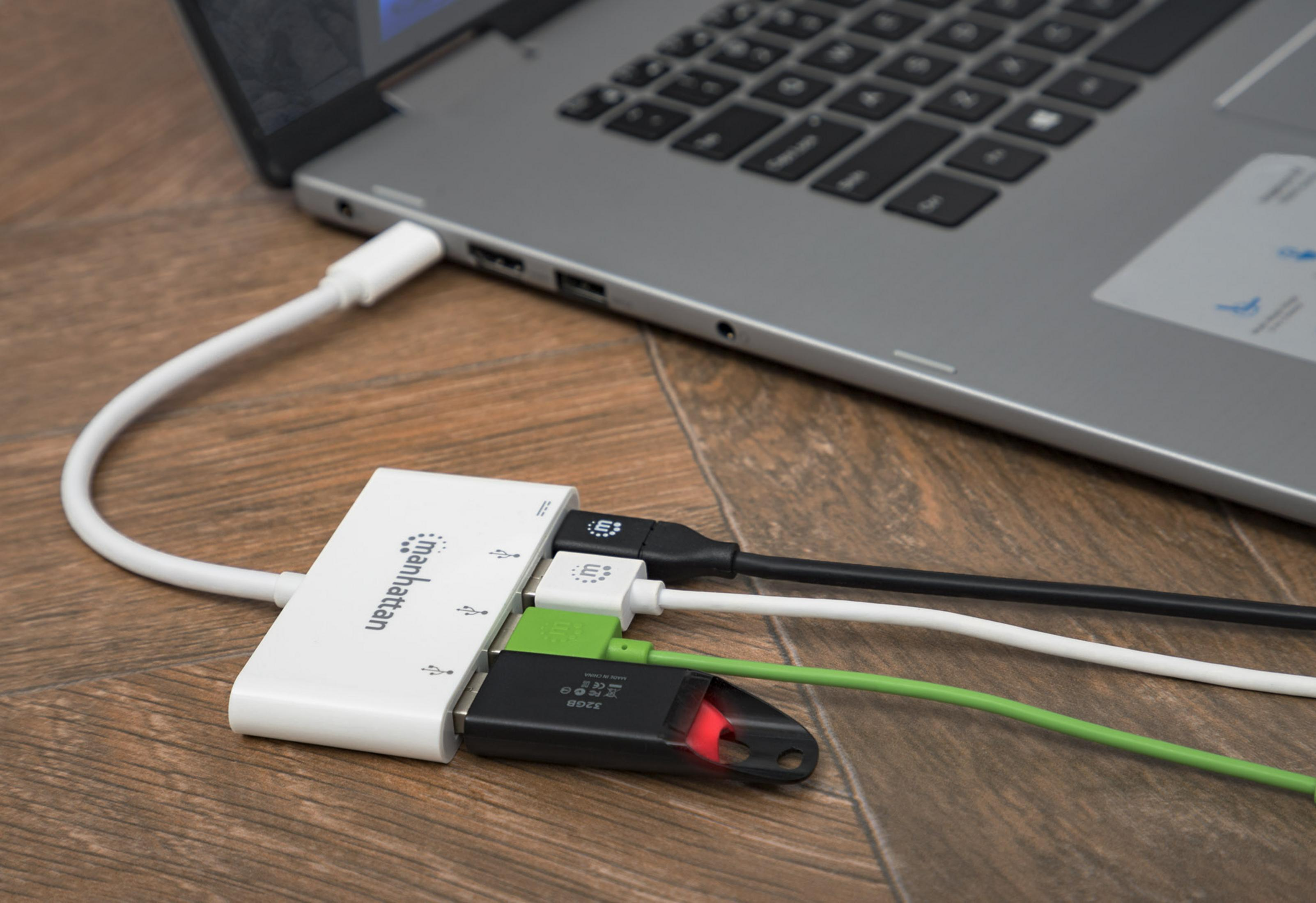 Un hub USB bianco con cavi e unità USB collegati, accanto a un laptop.