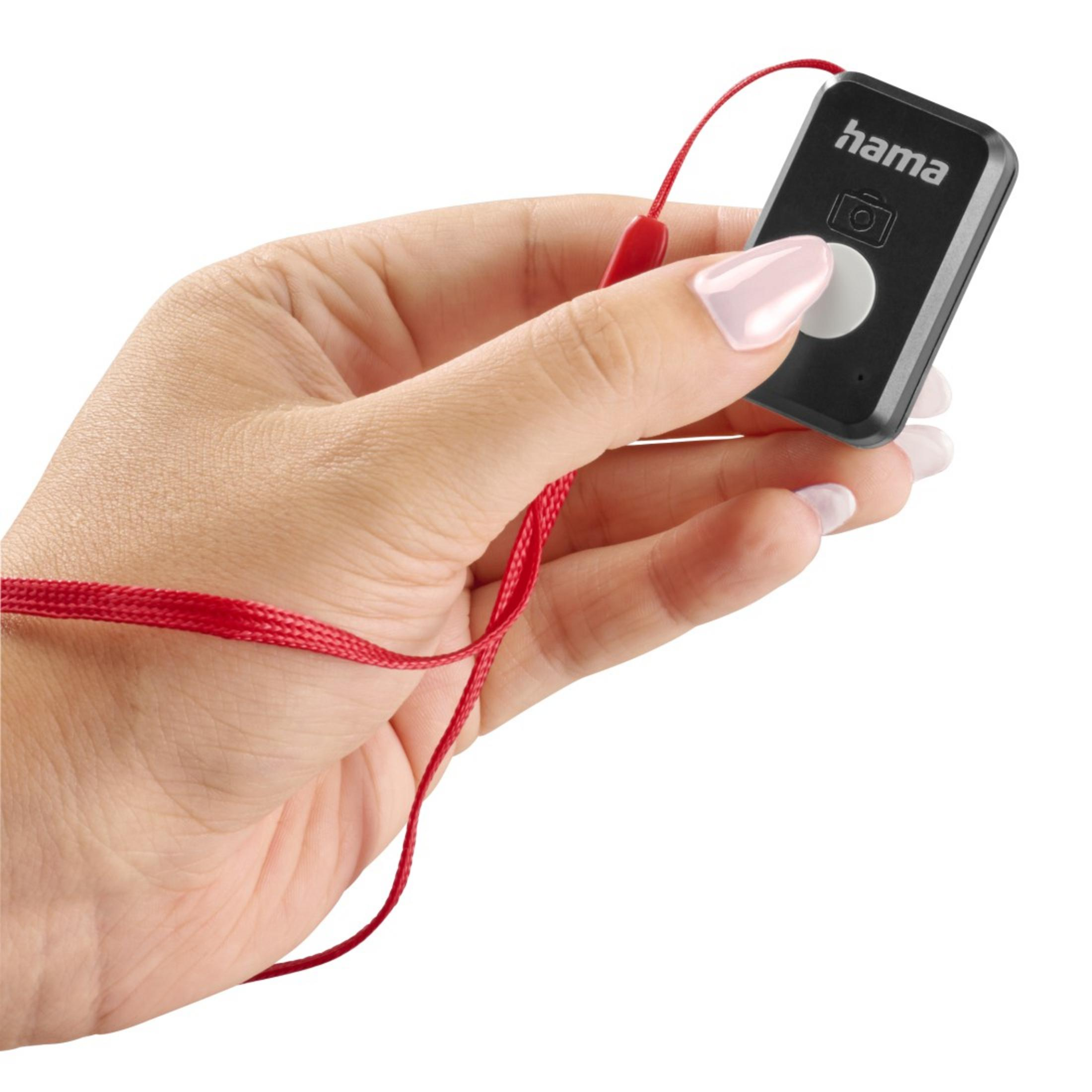 Una mano tiene un telecomando Hama nero con laccetto rosso.