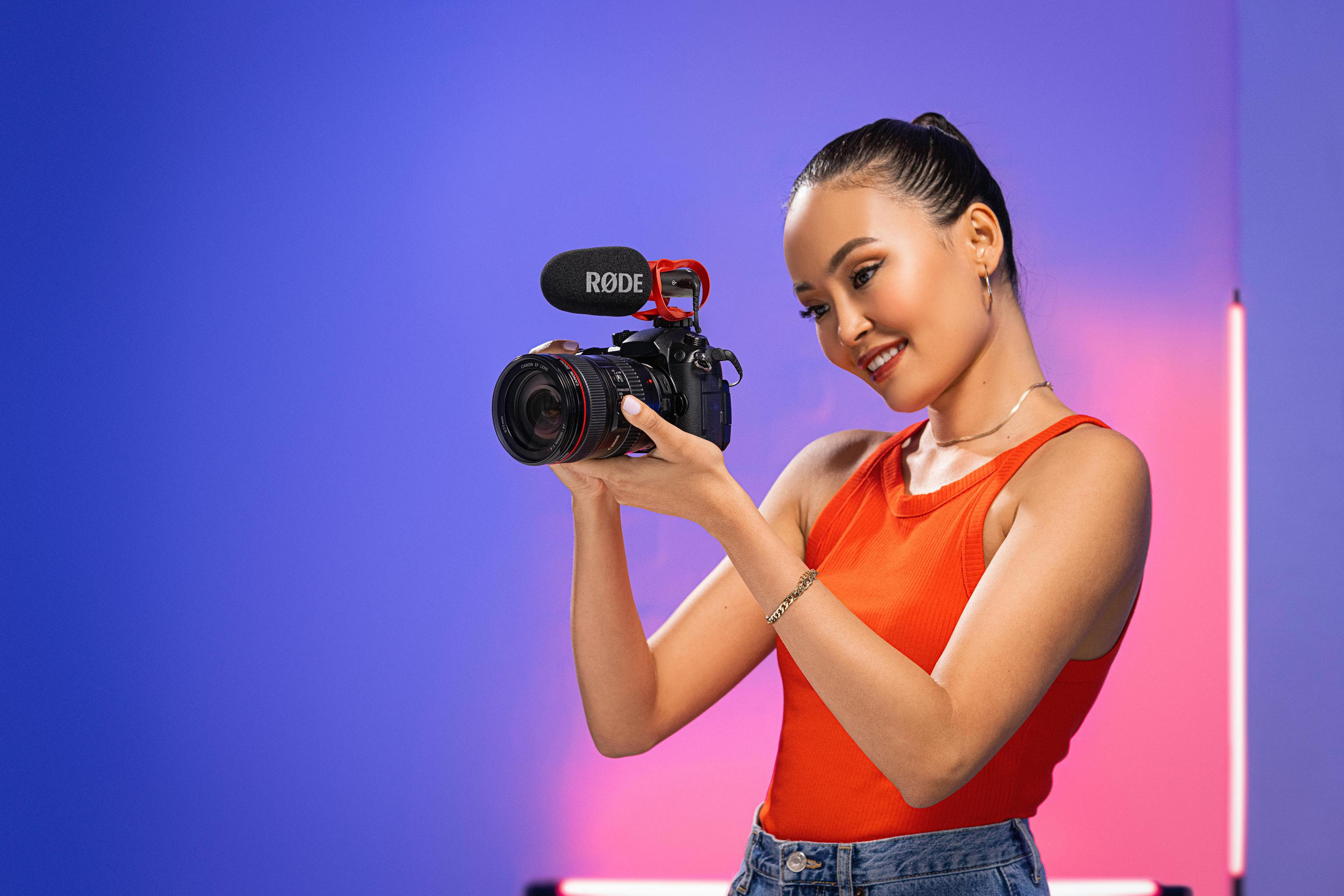 Una donna tiene una fotocamera con microfono su sfondo blu e rosa.
