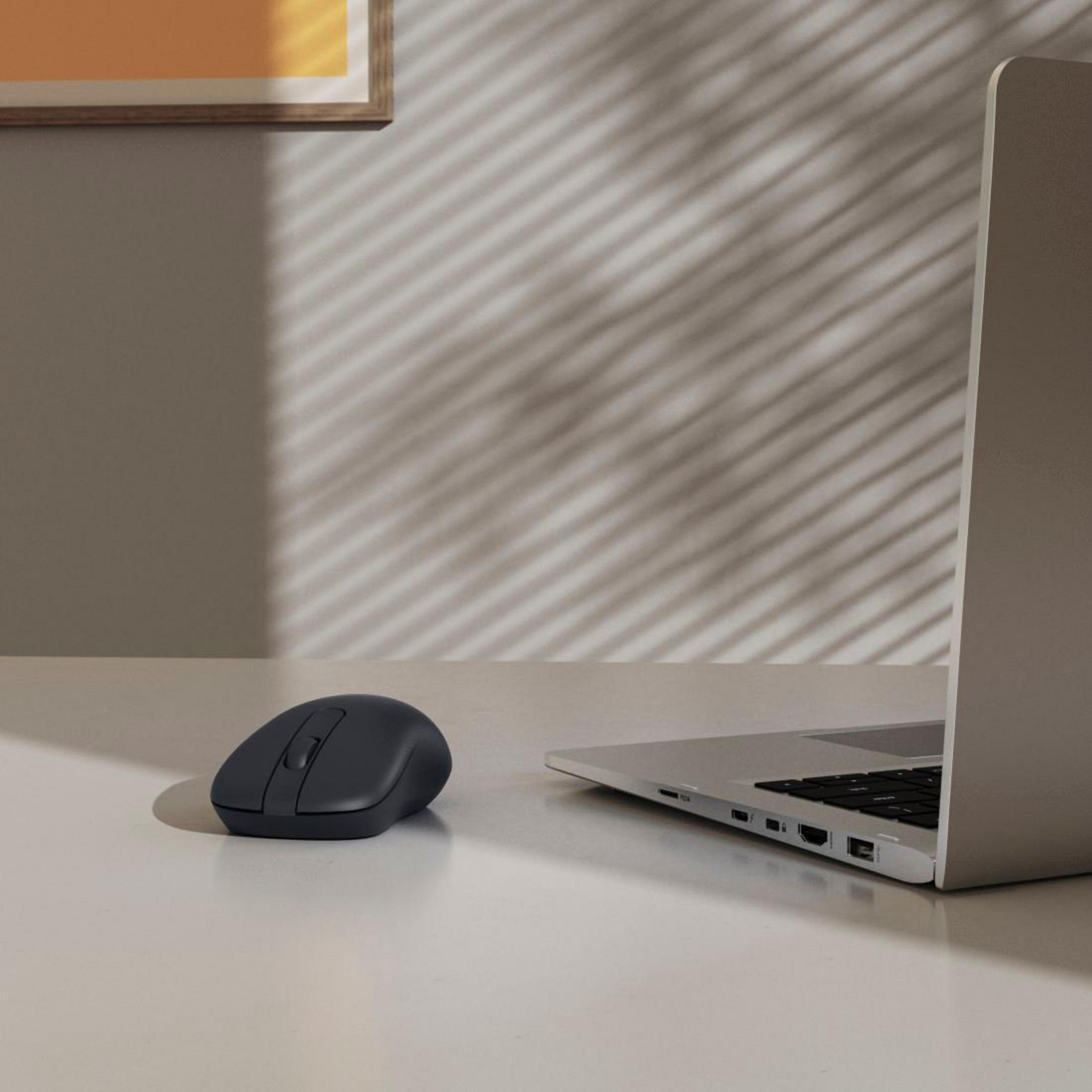 Un mouse scuro accanto a un laptop argentato su una scrivania chiara.
