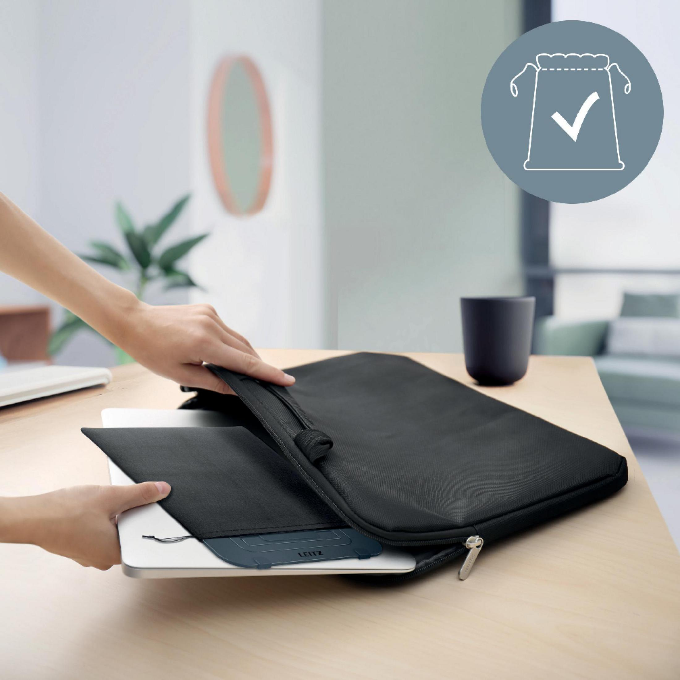 Persona inserisce laptop in custodia nera. Scrivania con tazza sullo sfondo.
