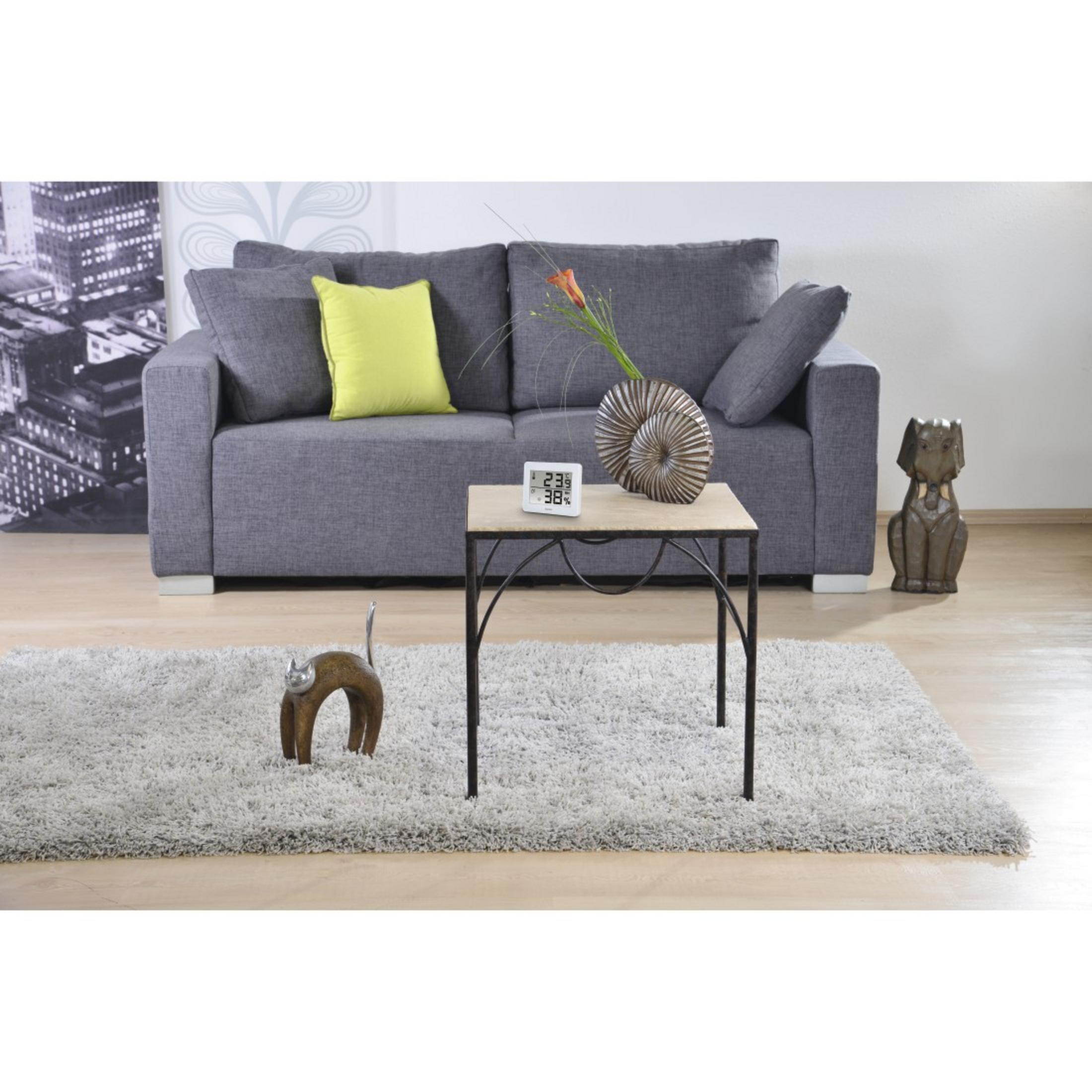 Szara sofa z poduszkami, stolik boczny z wazonem i termometrem, dywan.