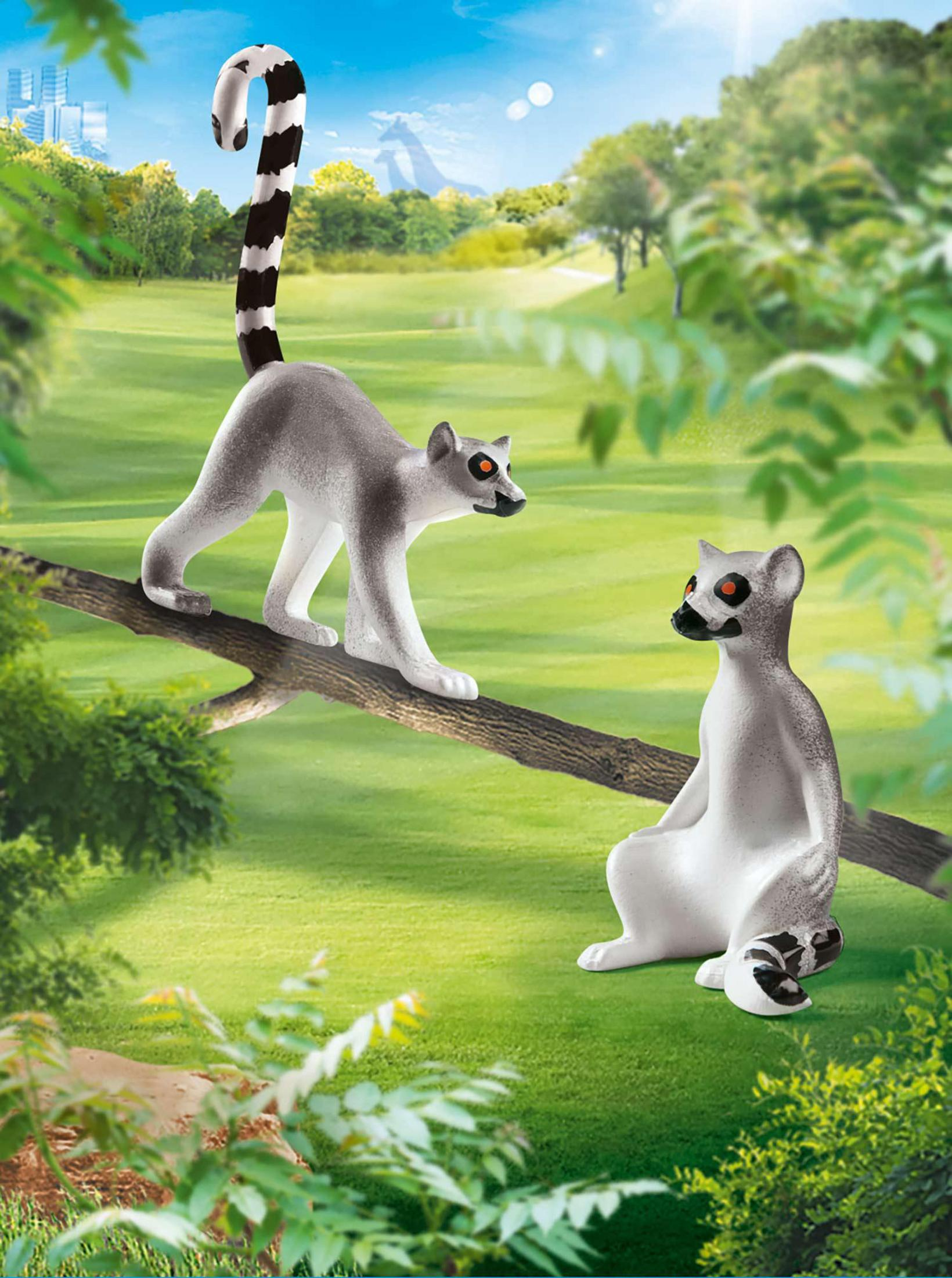 Due lemuri su un ramo in un paesaggio verde con alberi e cielo blu.