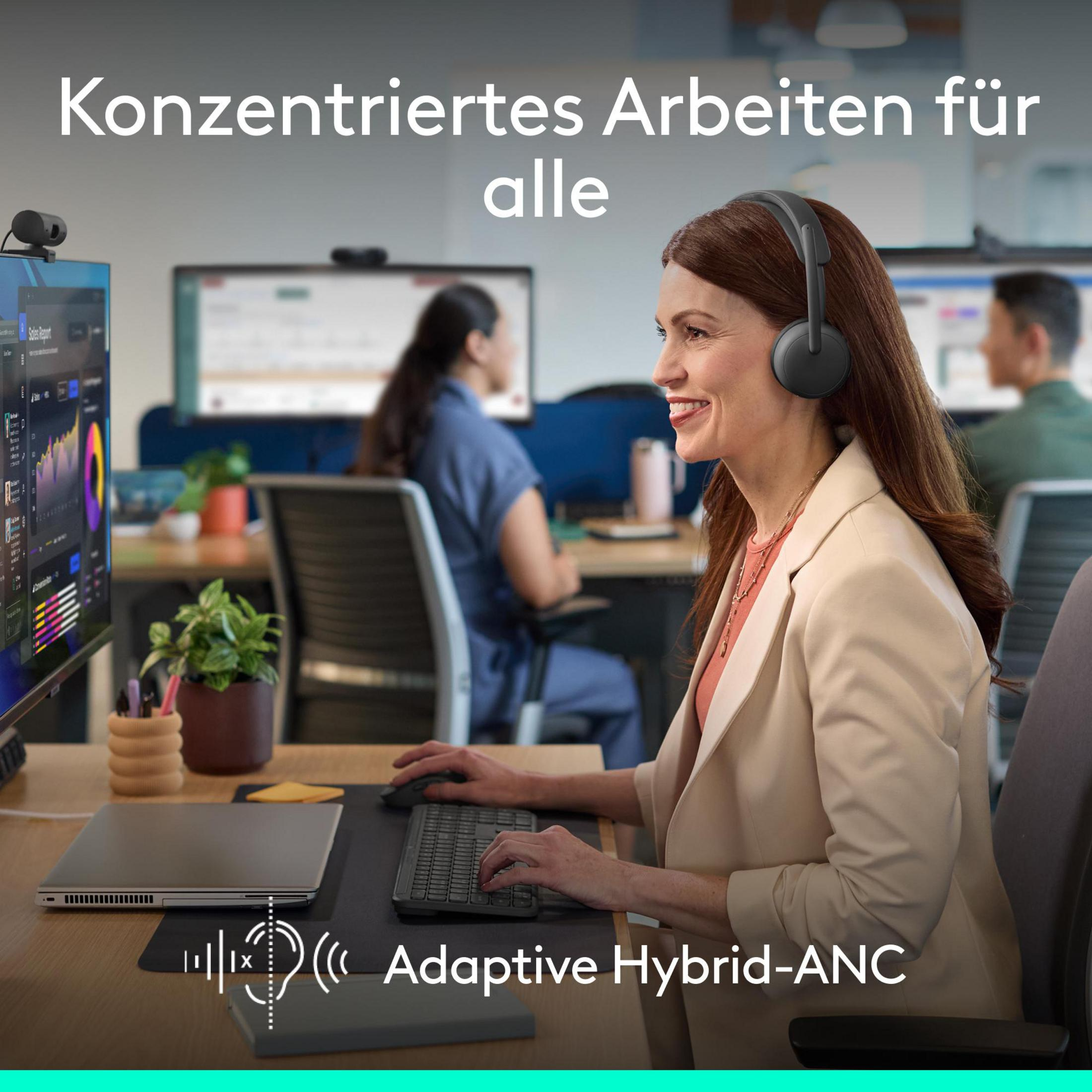 Woman wearing headphones works at a computer, colleagues in background.