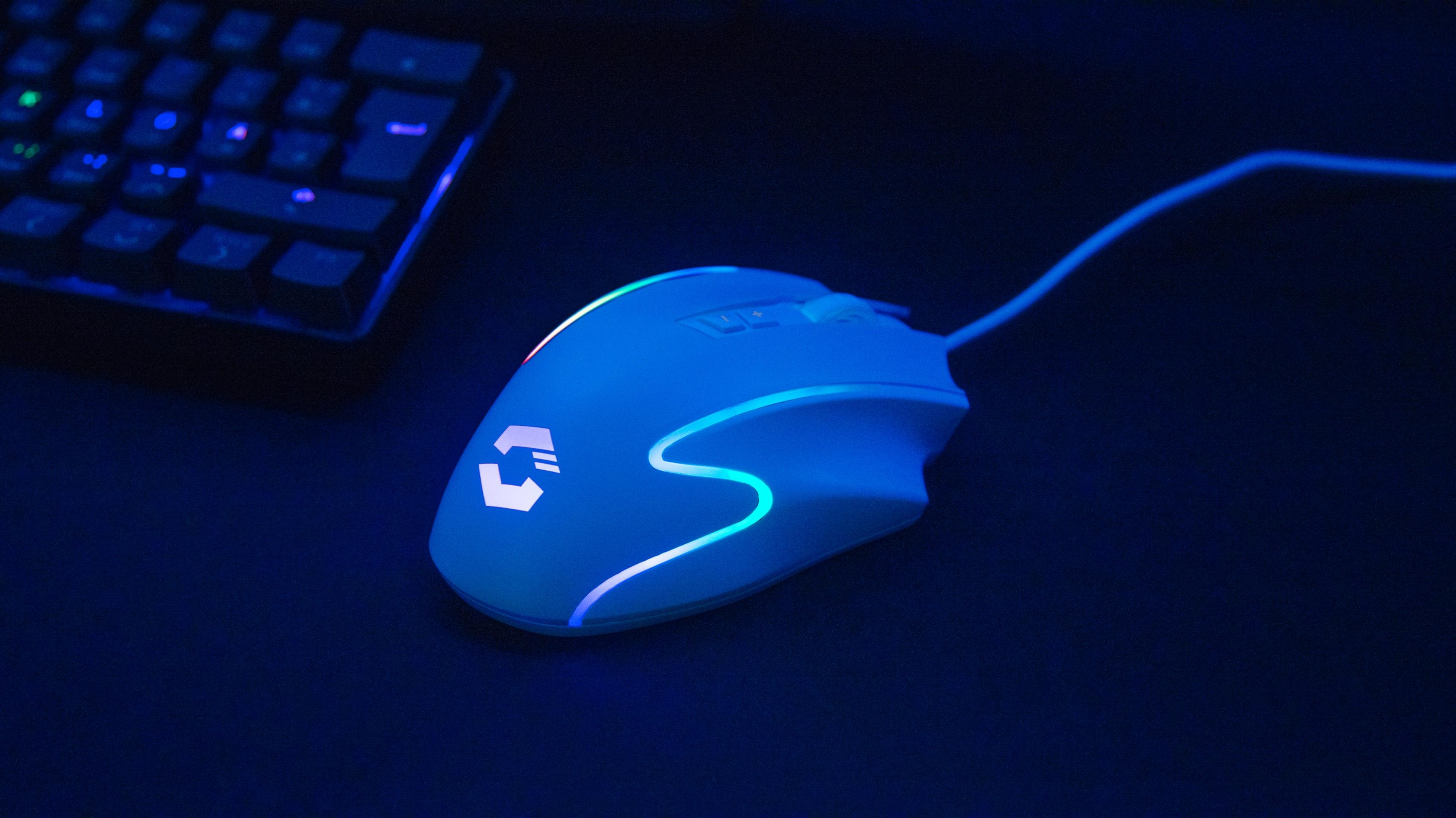 Un mouse da gioco bianco con illuminazione blu accanto a una tastiera.