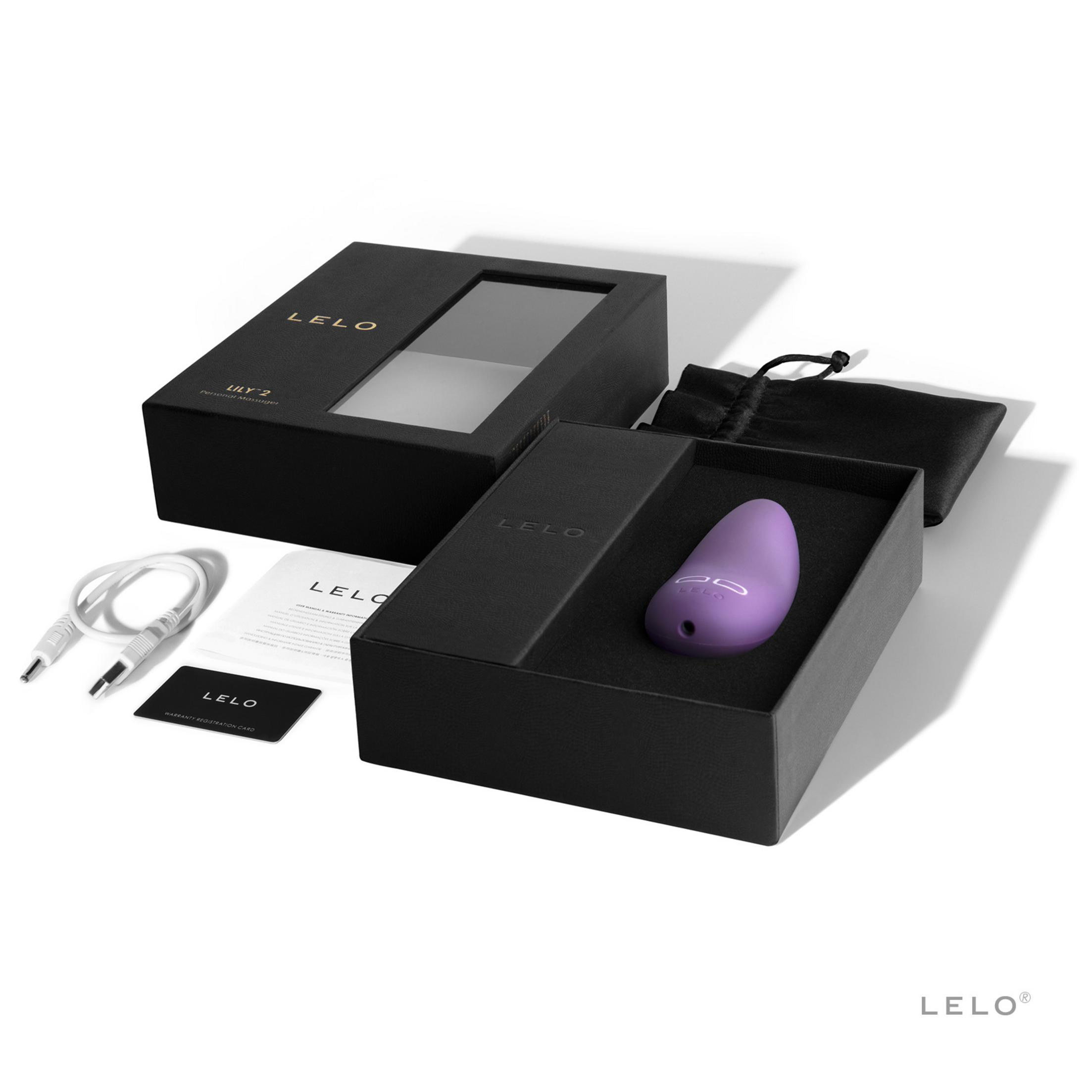 Masajeador morado en caja negra con cable, manual y tarjeta de garantía.