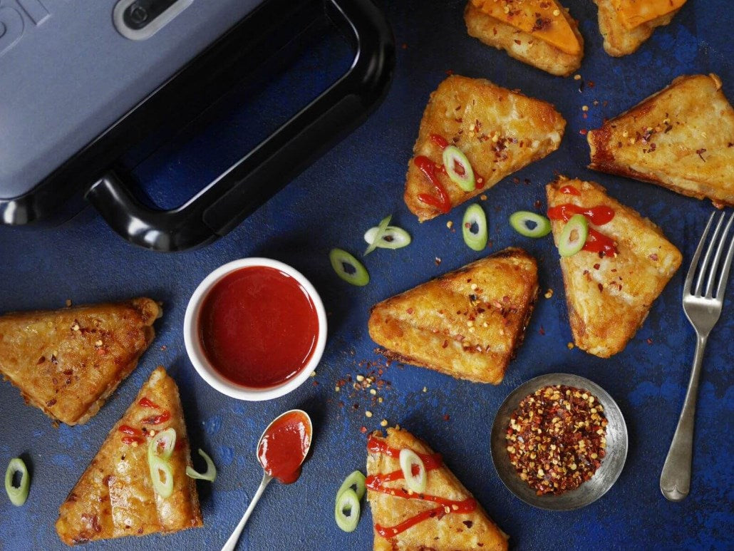 Sándwiches triangulares con kétchup, cebolletas y especias sobre fondo azul.