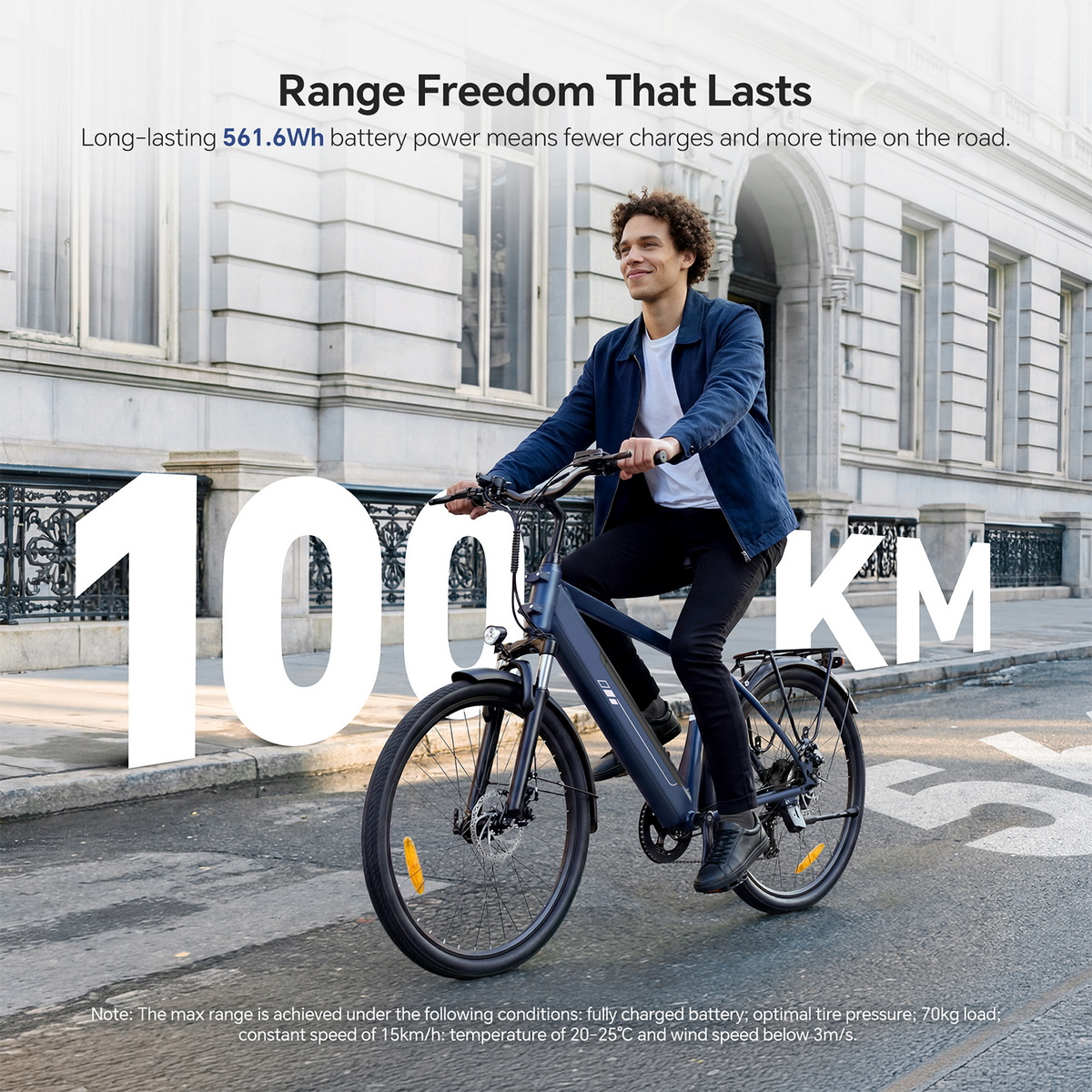 Mężczyzna jadący ciemnoniebieskim rowerem elektrycznym po ulicy miasta. Duży biały napis: '100 KM'.