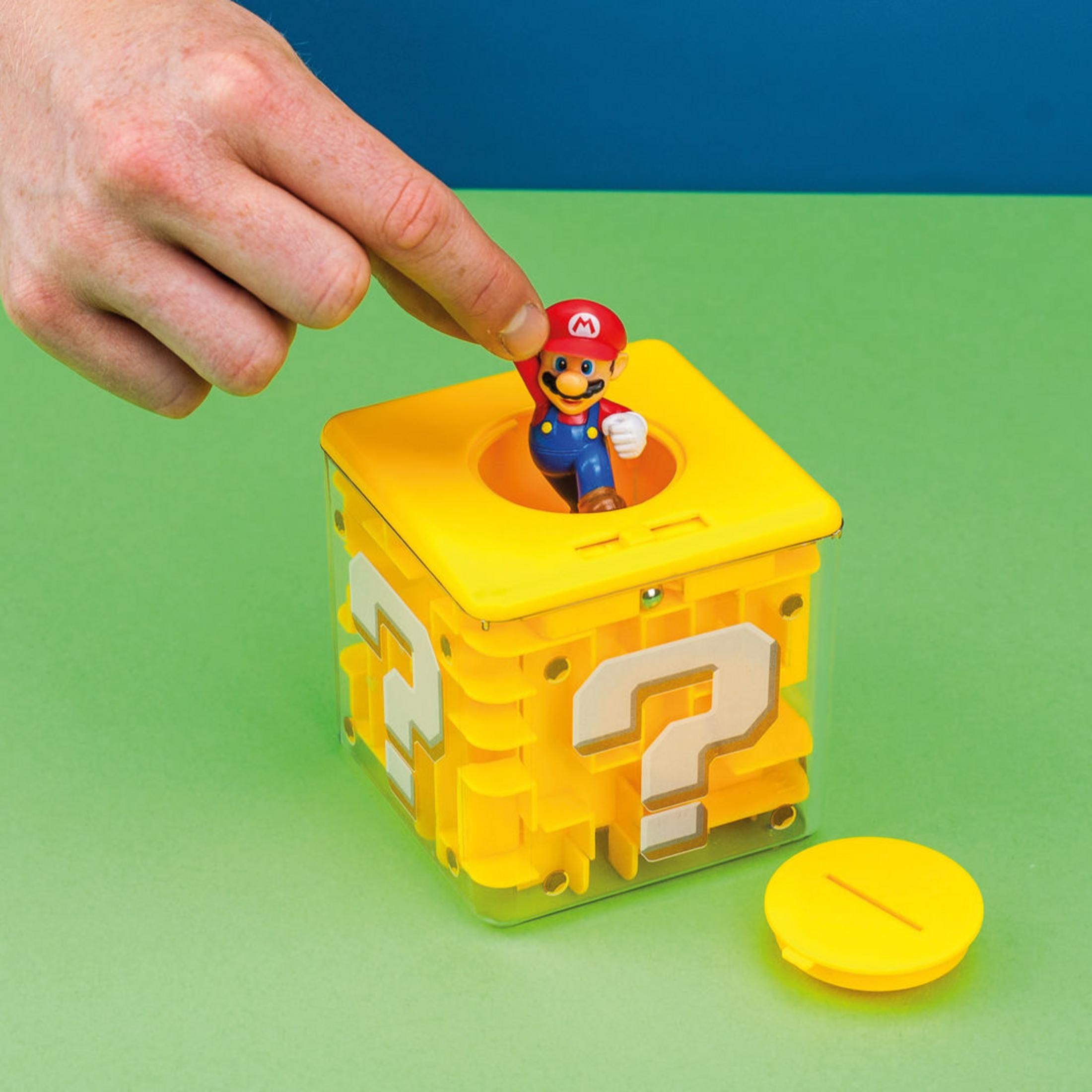 Una persona coloca una figura de Mario en un cubo amarillo de signo de interrogación sobre superficie verde.
