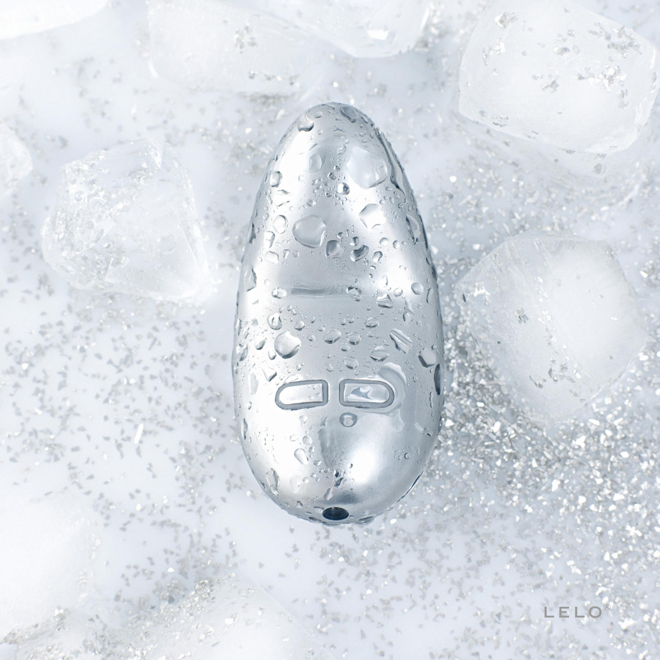 Ein silbernes Objekt mit Wassertropfen liegt auf Eiswürfeln und Glitzer.