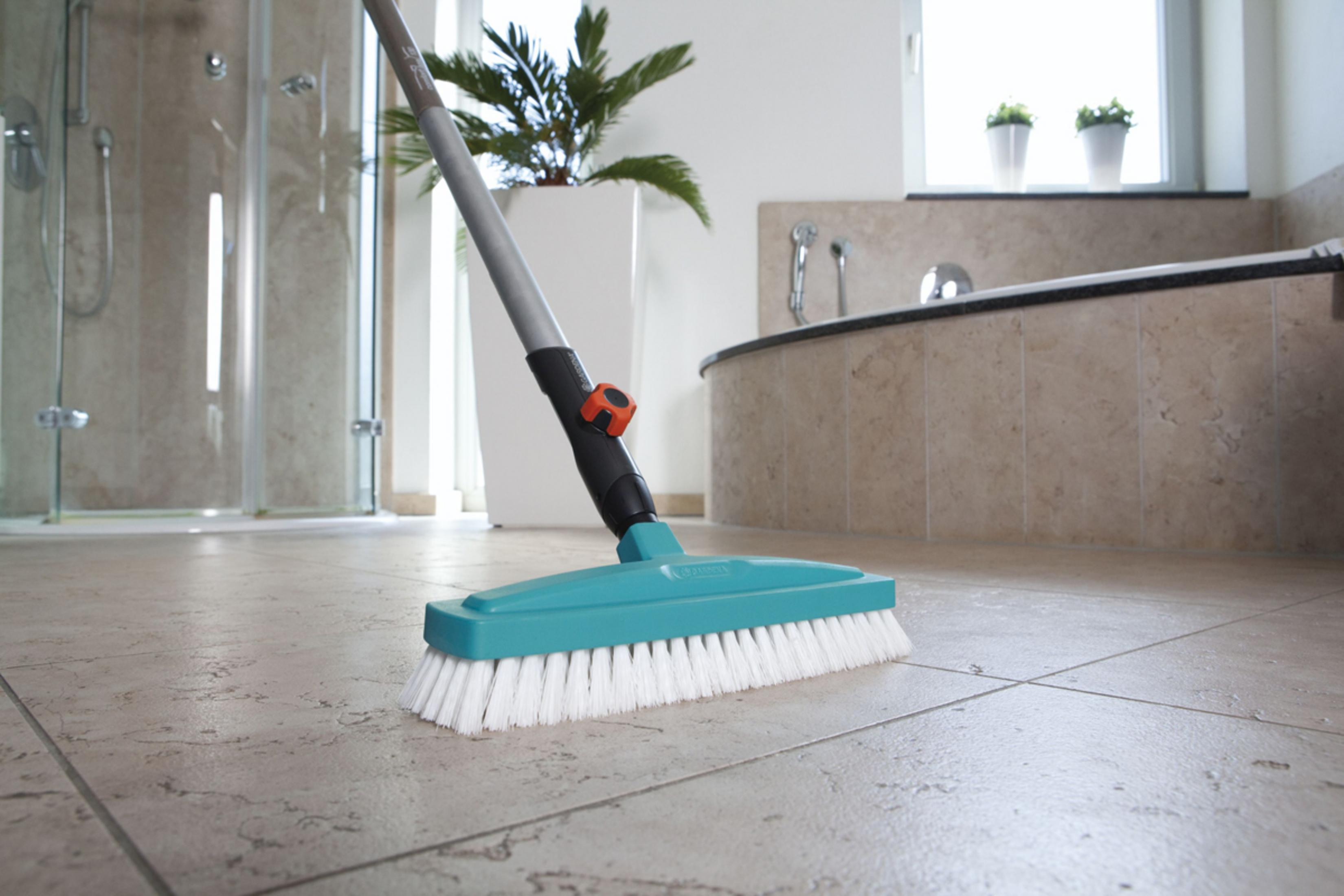 Una spazzola turchese con setole bianche pulisce un pavimento piastrellato del bagno.