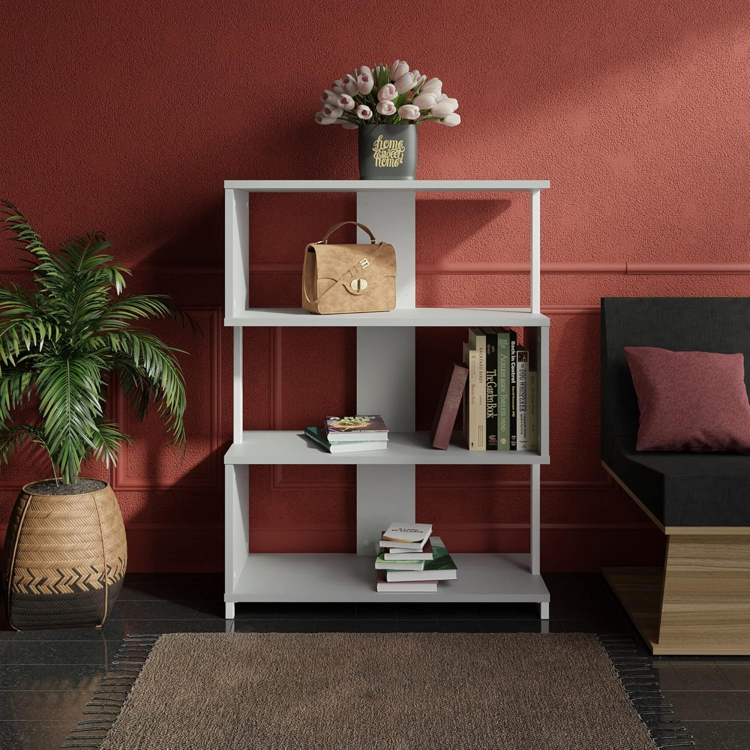 Una estantería blanca con libros, un bolso y flores contra una pared roja texturizada.
