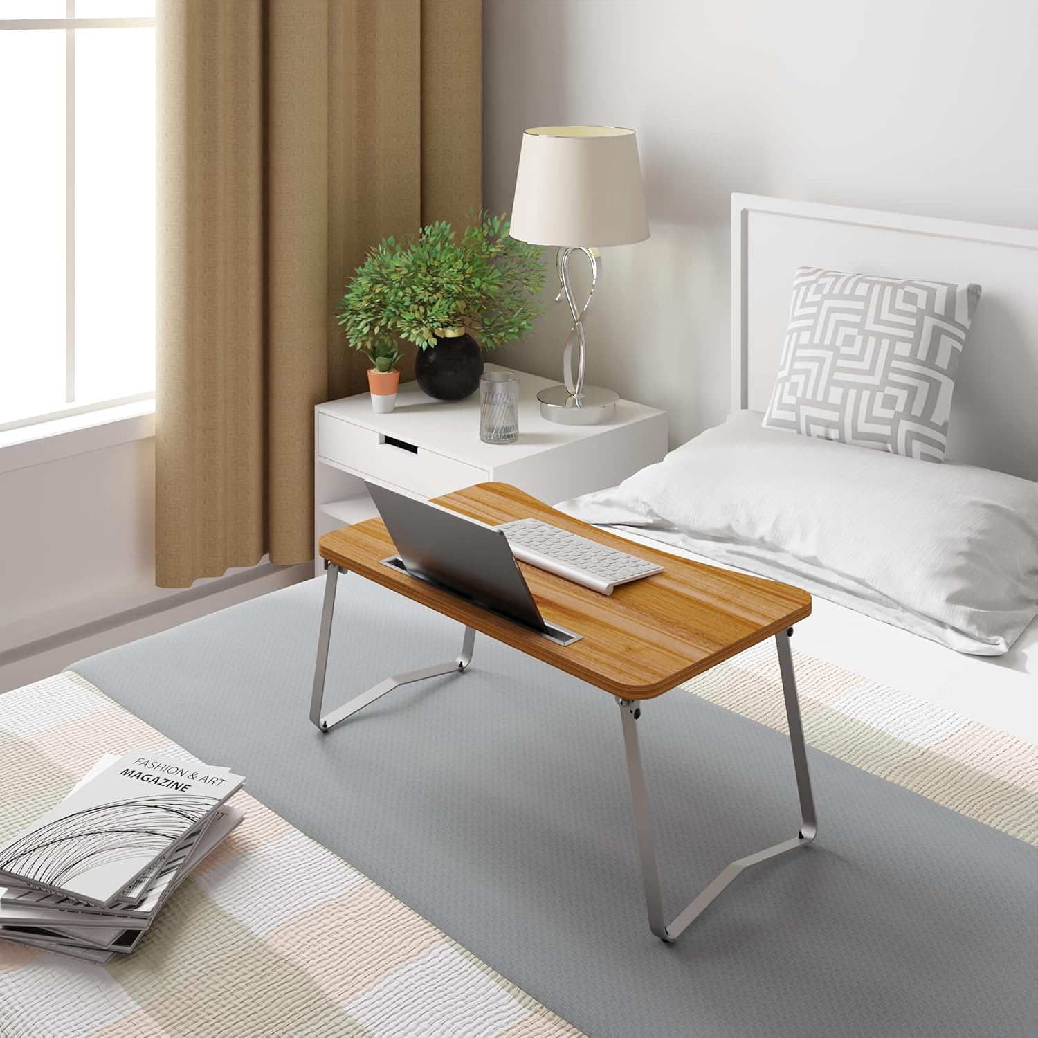Un portátil sobre una mesa de madera con patas plegables en una cama.