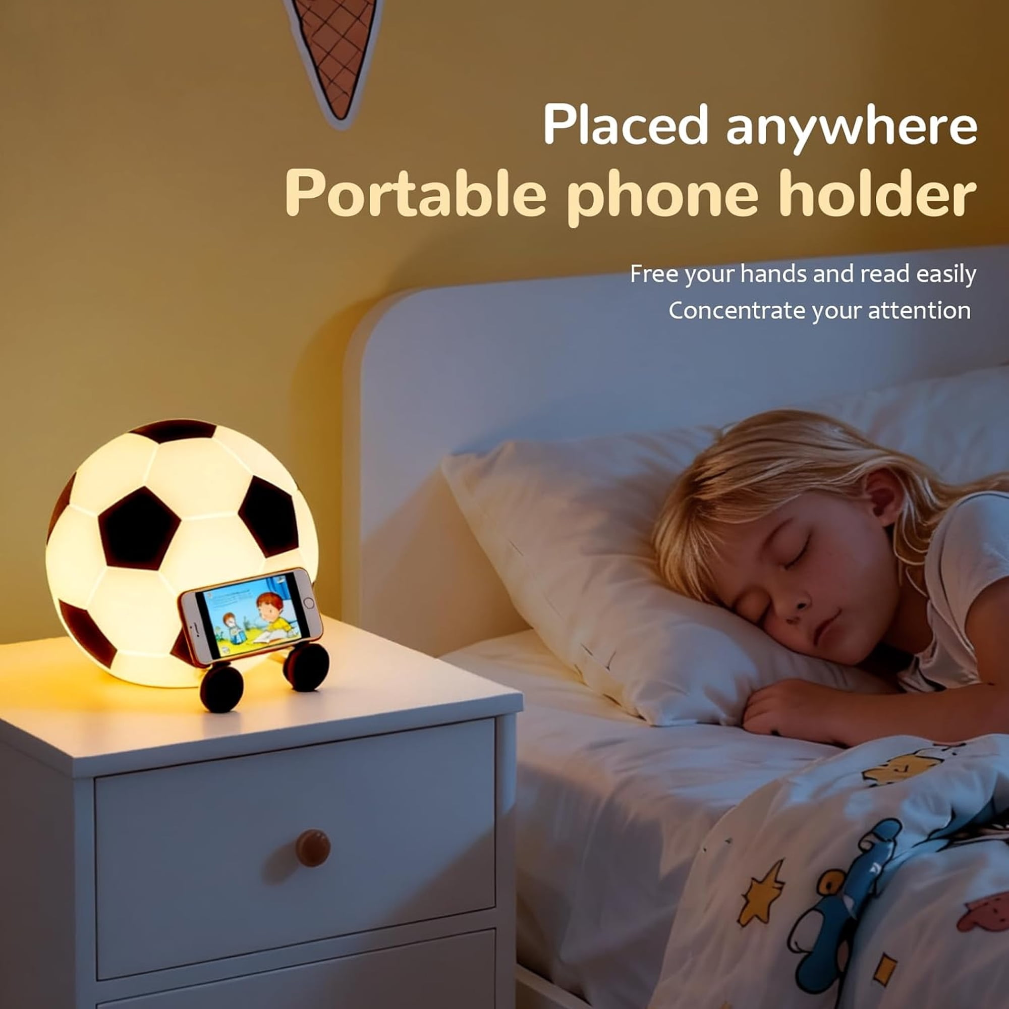 Ein Nachttisch mit einem fußballförmigen Nachtlicht und einem Handyhalter. Ein Kind schläft im Bett.
