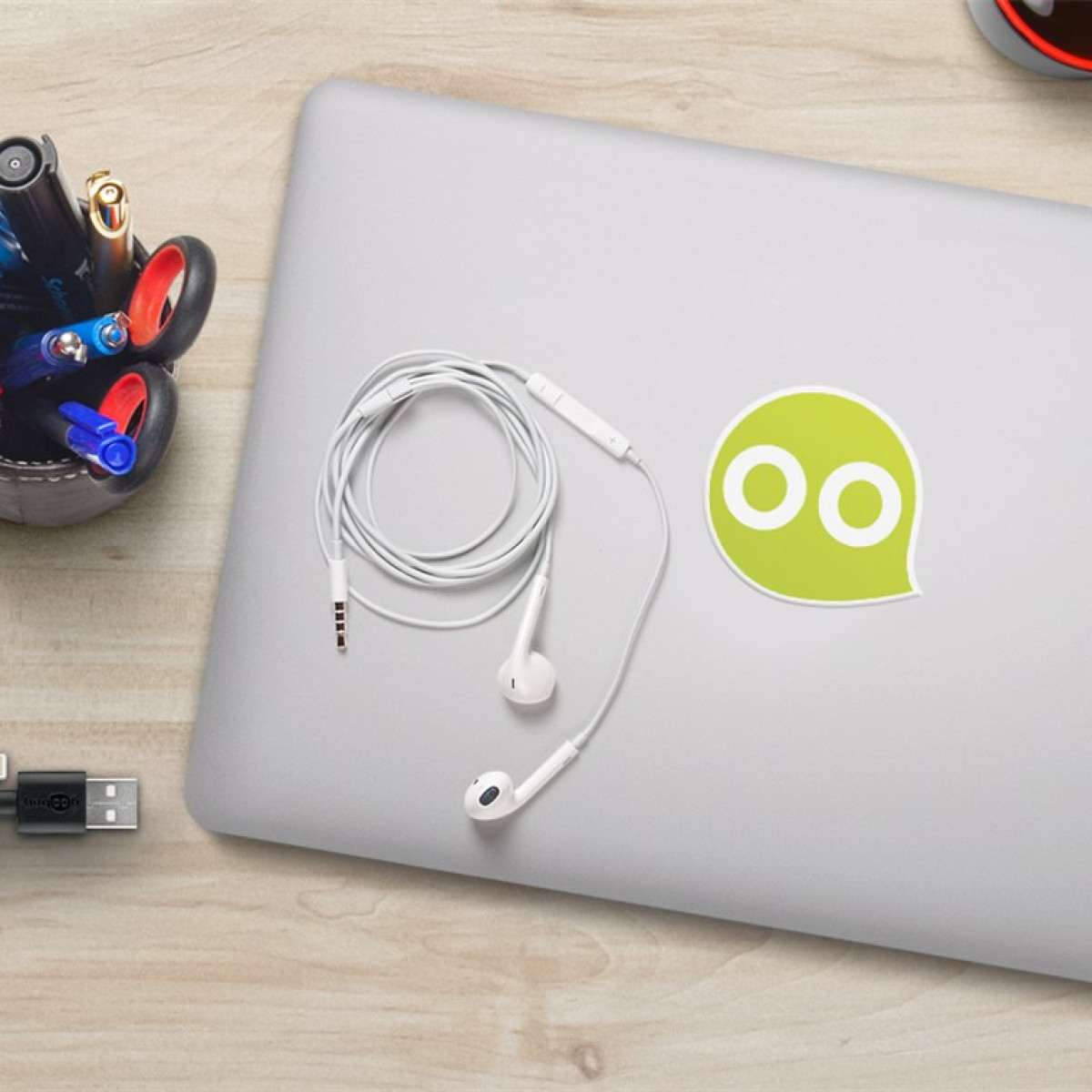 Weiße Ohrhörer auf einem Laptop mit grünem Logo, Stiftehalter und USB-Kabel.