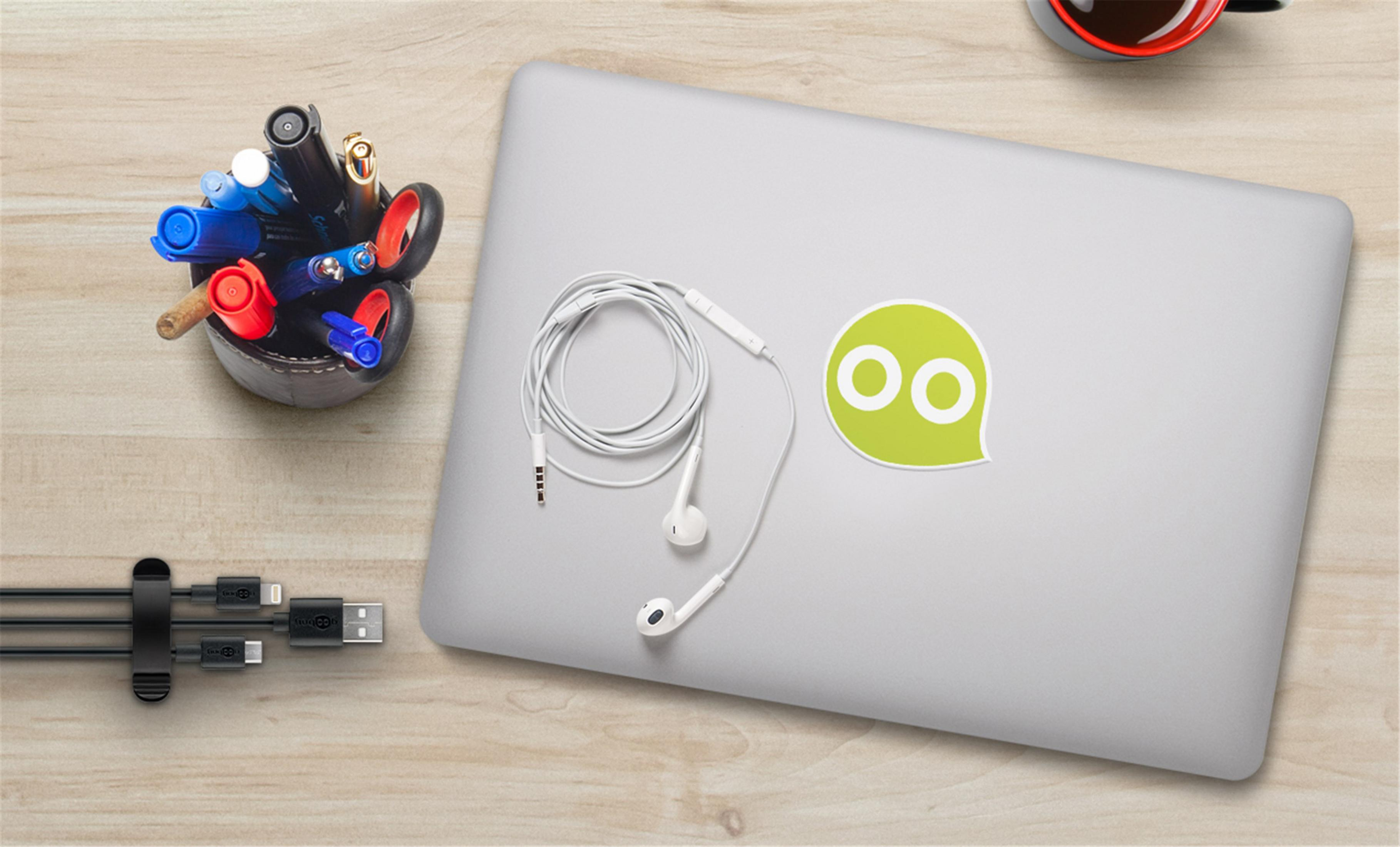 Laptop mit Kopfhörern, Stiftehalter und Ladekabeln auf Holztisch.