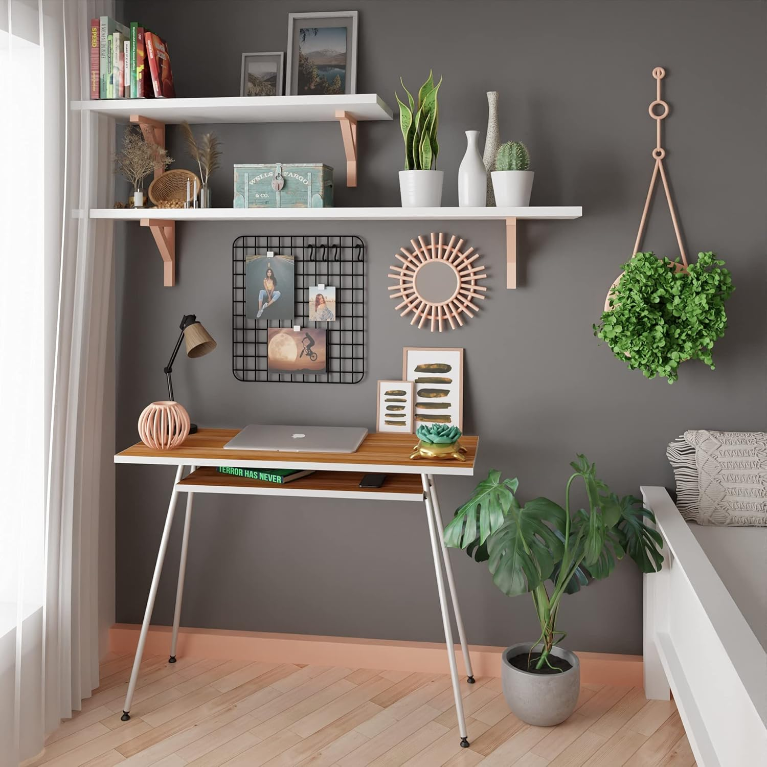 Un escritorio con laptop, lámpara y plantas frente a una pared con estantes.