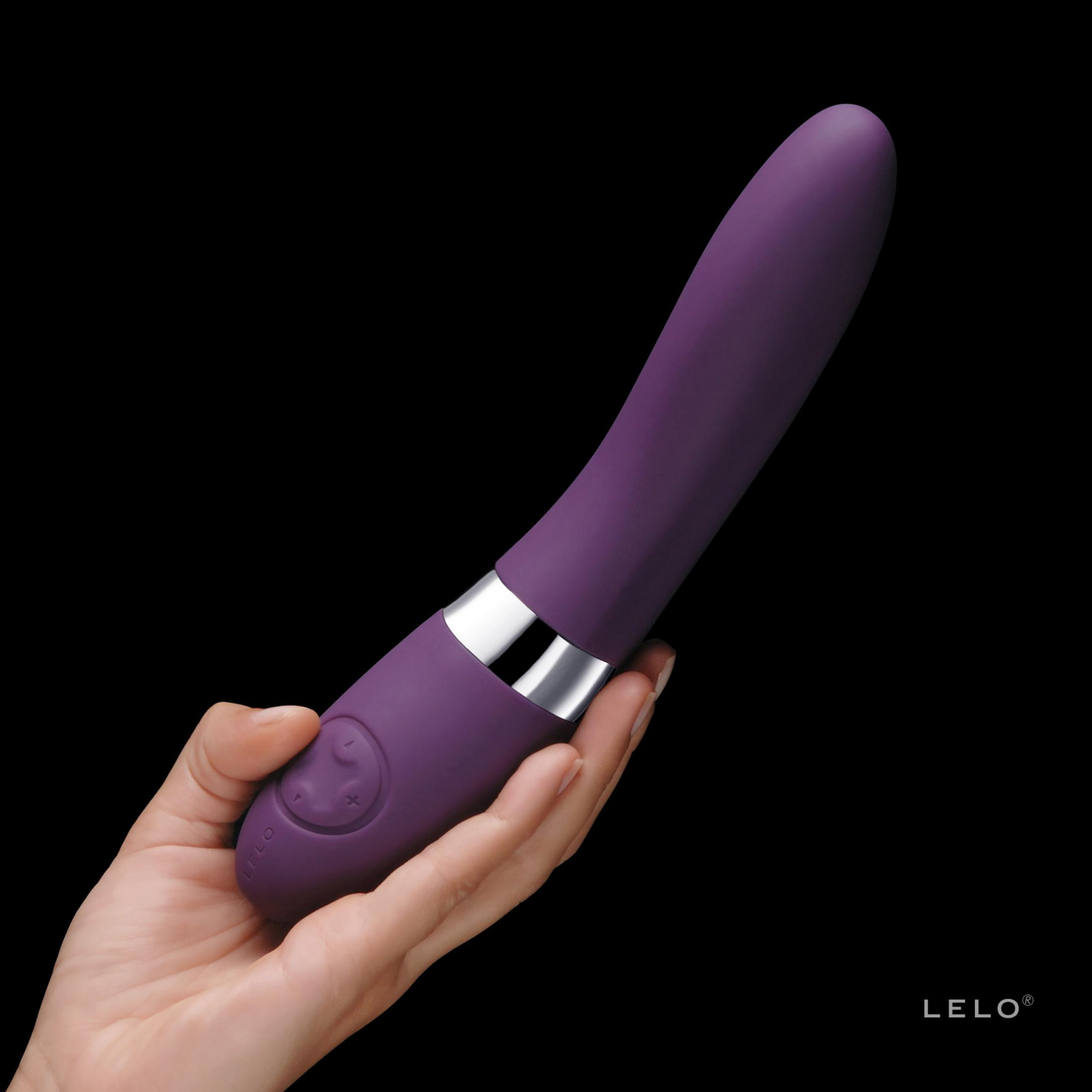 Una mano sostiene un vibrador morado con anillos plateados.