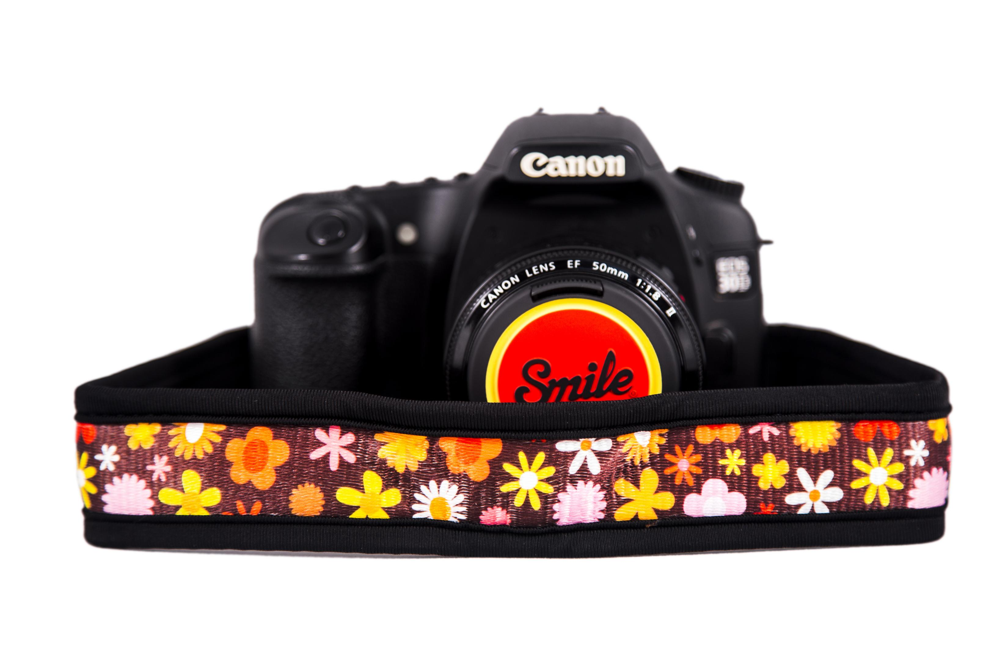 Fotocamera Canon nera con tappo obiettivo "Smile" su tracolla floreale.